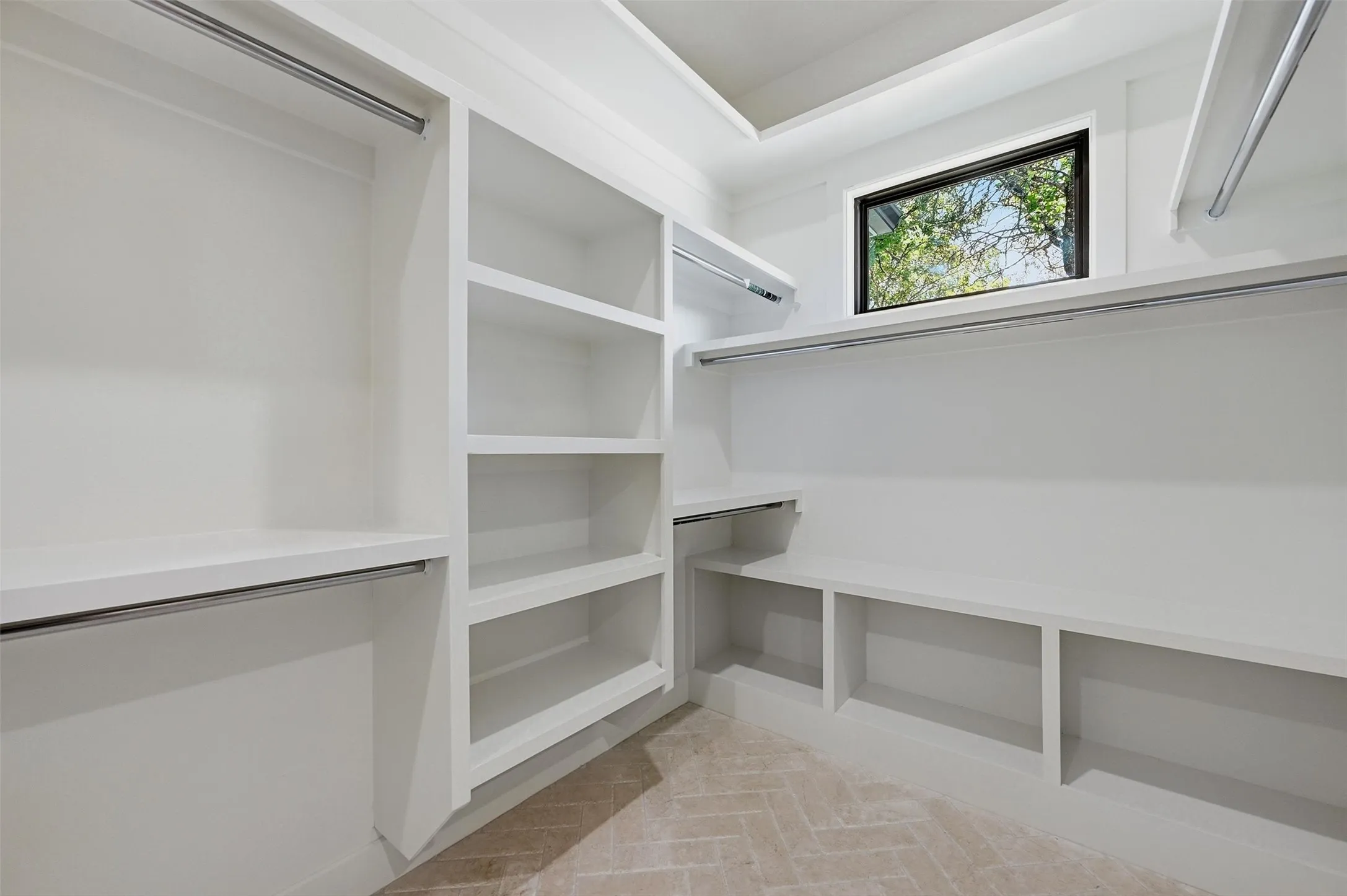 White built-in shelving, multiple hanging rods, recessed lighting, herringbone-patterned flooring, and a single window