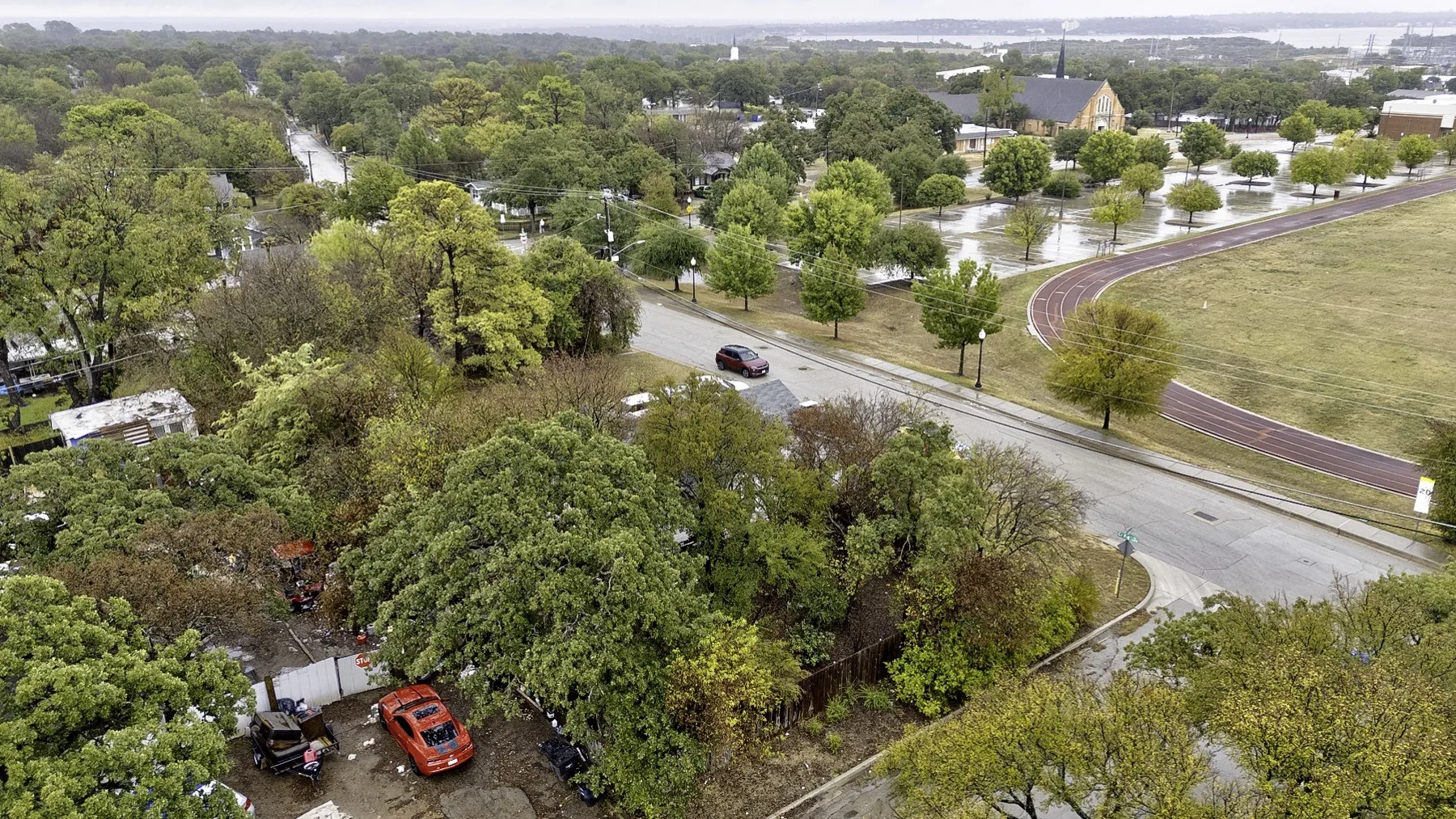 Aerial along the side street past the corner lot's mature tree canopy, looking into the Handley neighborhood