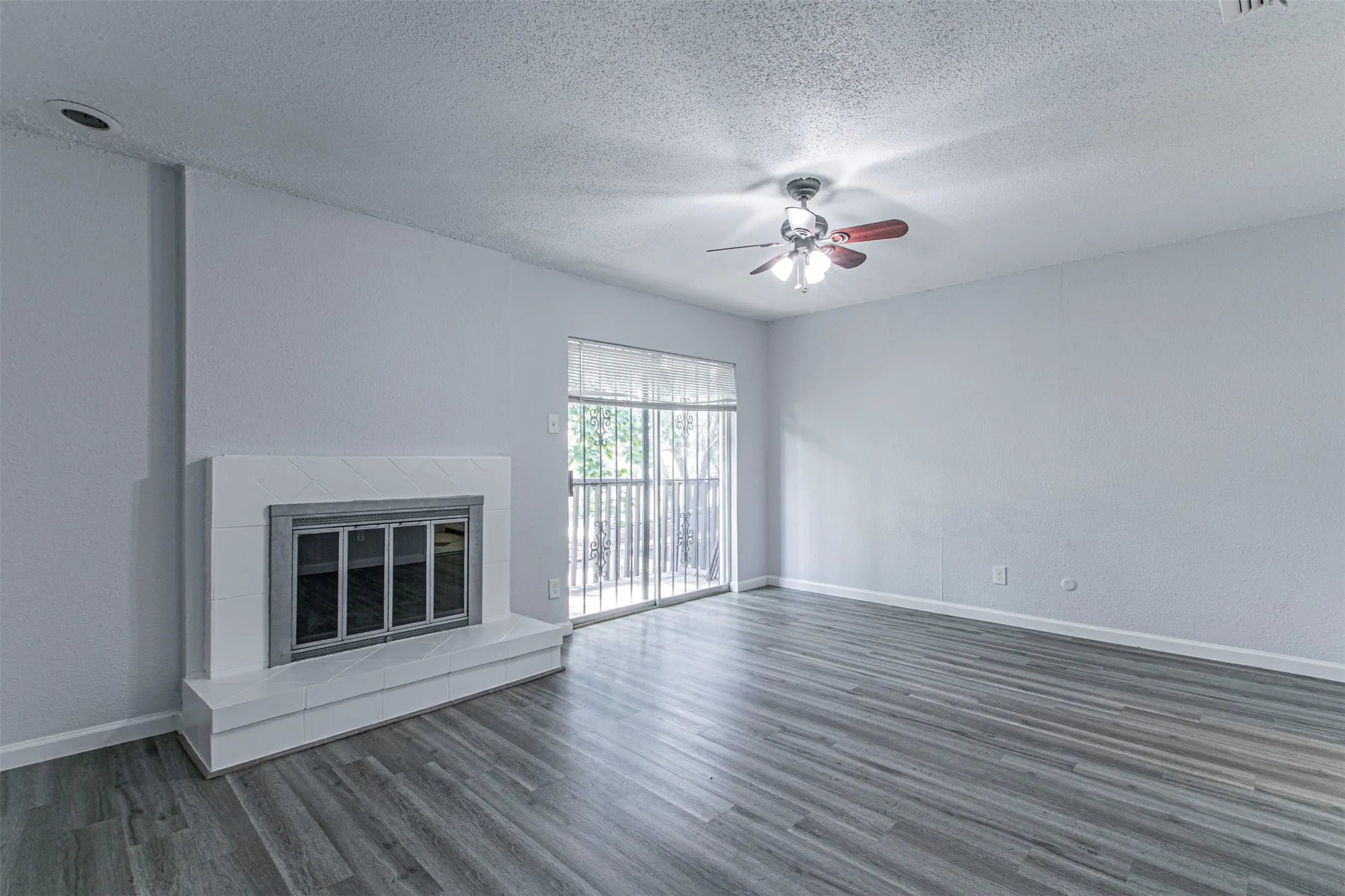 Bedroom 3 - Unfurnished living room featuring a tile fireplace, dark wood finished floors, a textured ceiling, and ceiling fan