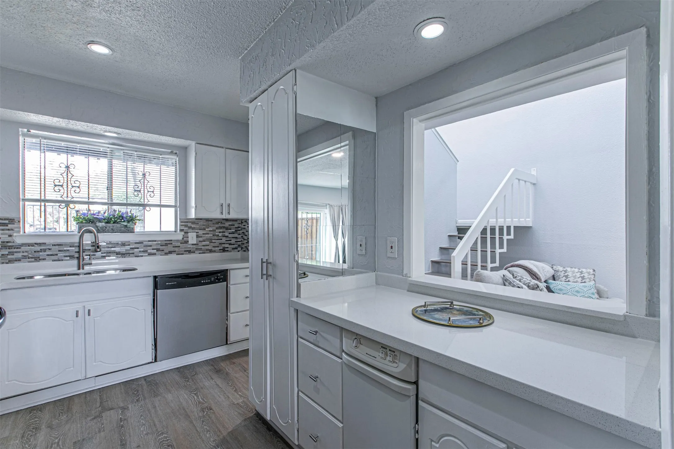 Kitchen featuring a textured ceiling, dishwasher, white cabinetry, light wood-type flooring, and light stone counters