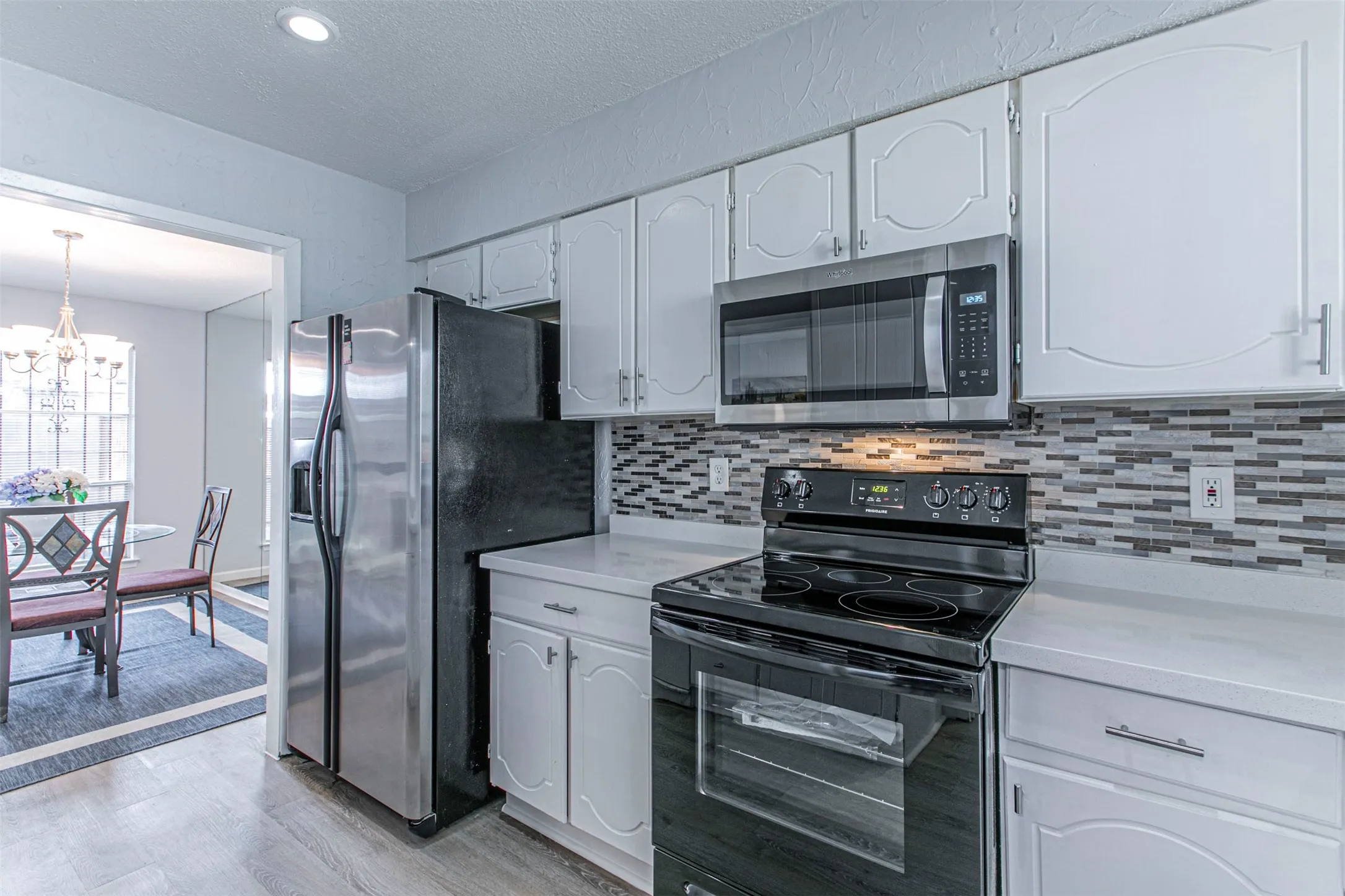 Kitchen with appliances with stainless steel finishes, light wood-style flooring, backsplash, a chandelier, and a textured ceiling