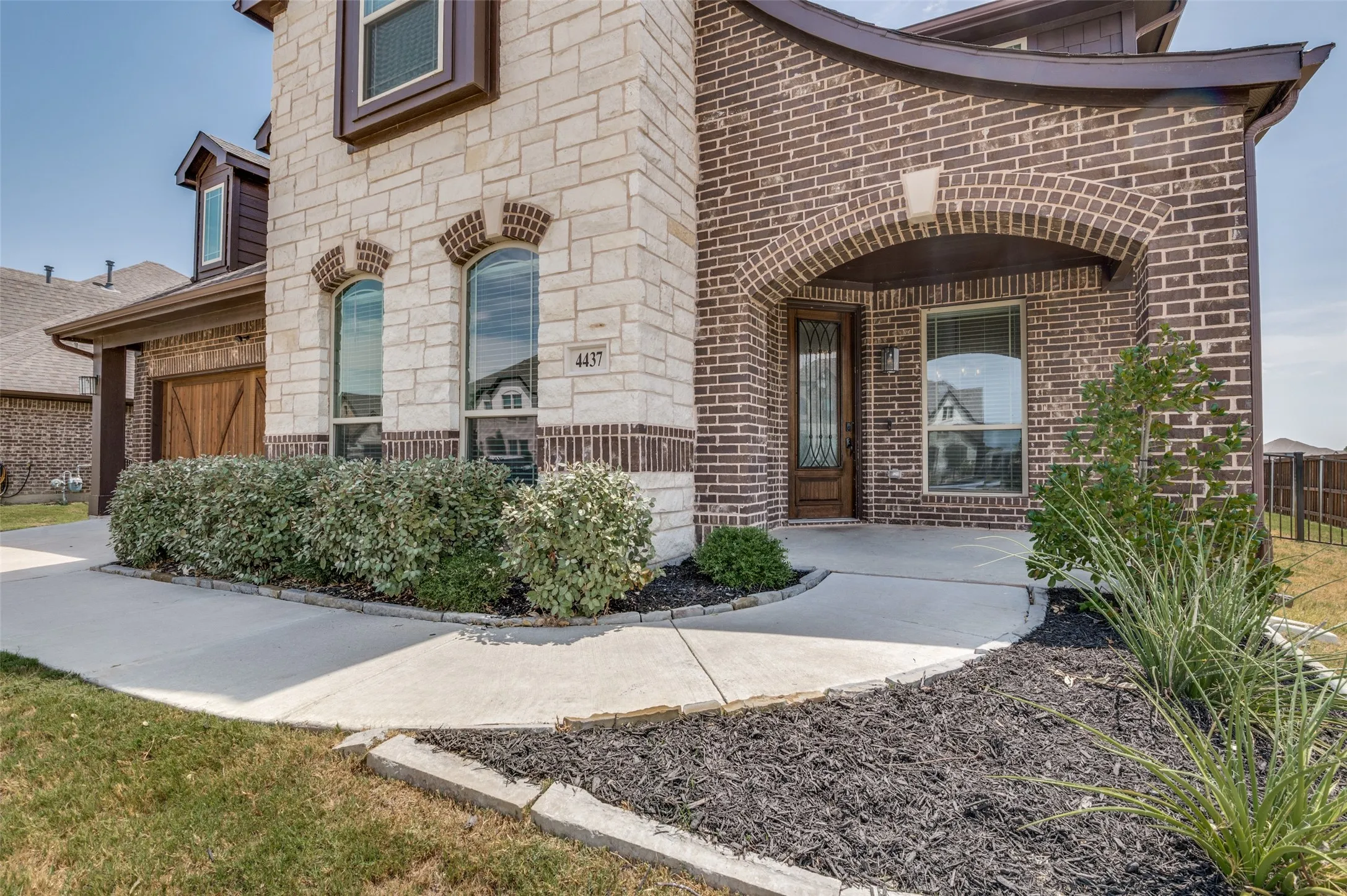 Stone and brick exterior with arched entry, arched windows, covered porch, and wood paneled garage door