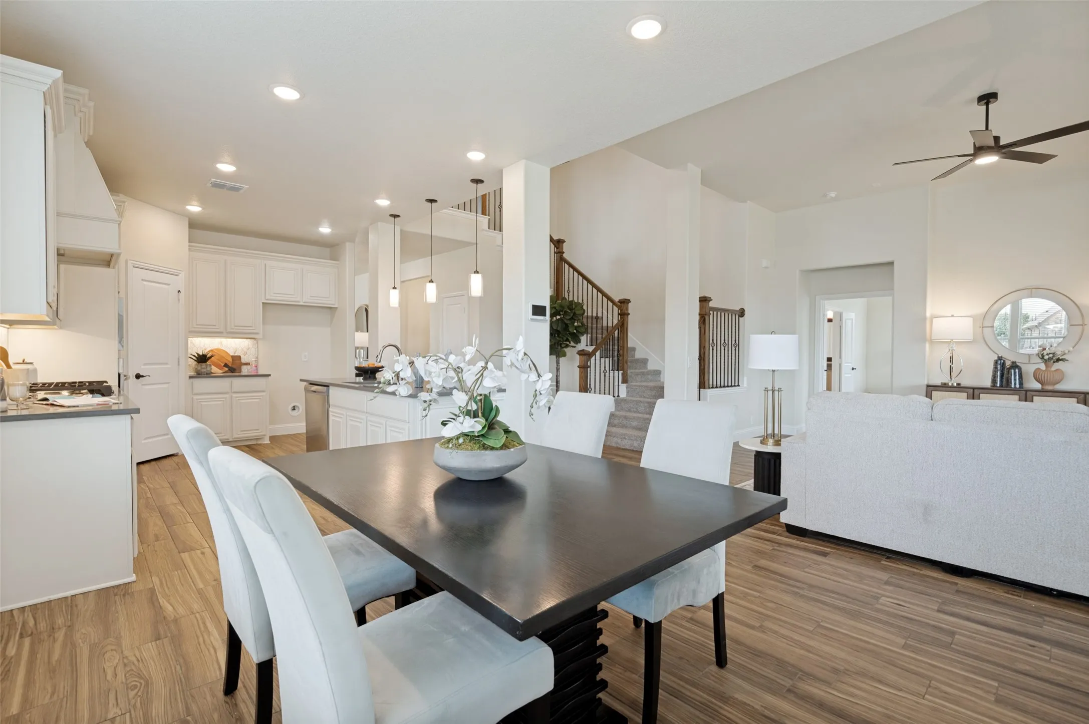 Open concept living space featuring wood-finish flooring, a kitchen with white cabinetry and an island, and a staircase with wooden handrails