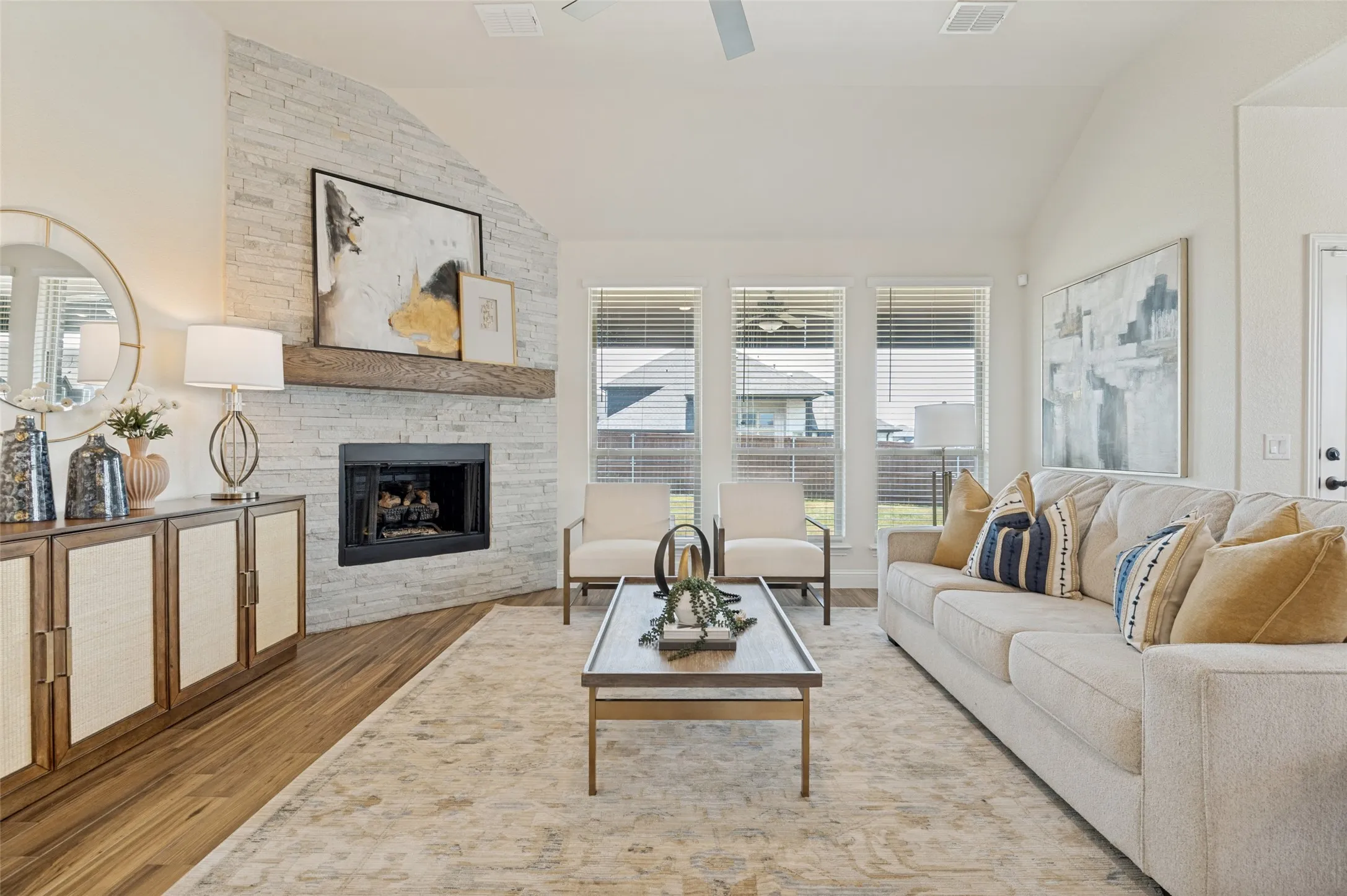 Vaulted ceiling, stone fireplace with a wood mantel, wood-finish flooring, and multiple windows