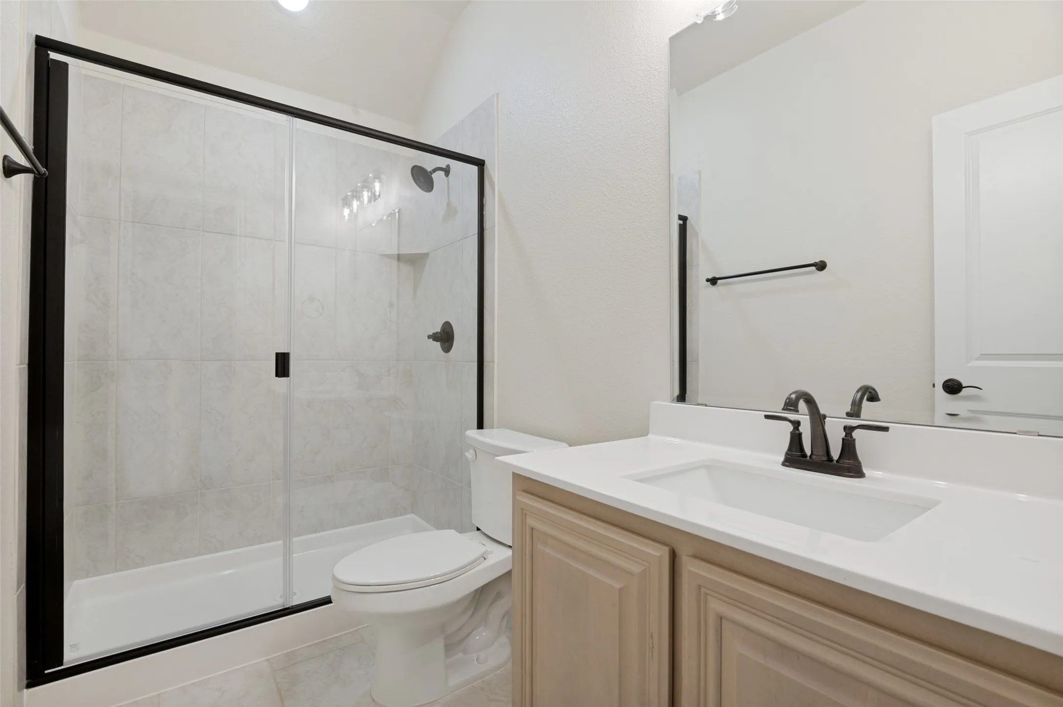 Shower with black-framed glass enclosure, tile surround, and dark-finished fixtures