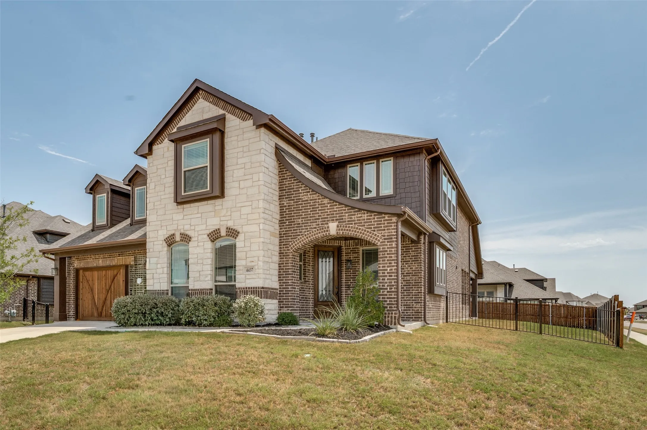 Two-story exterior featuring brick and stone masonry, a covered arched entry, dormer windows, and an attached garage with a wood-finish door