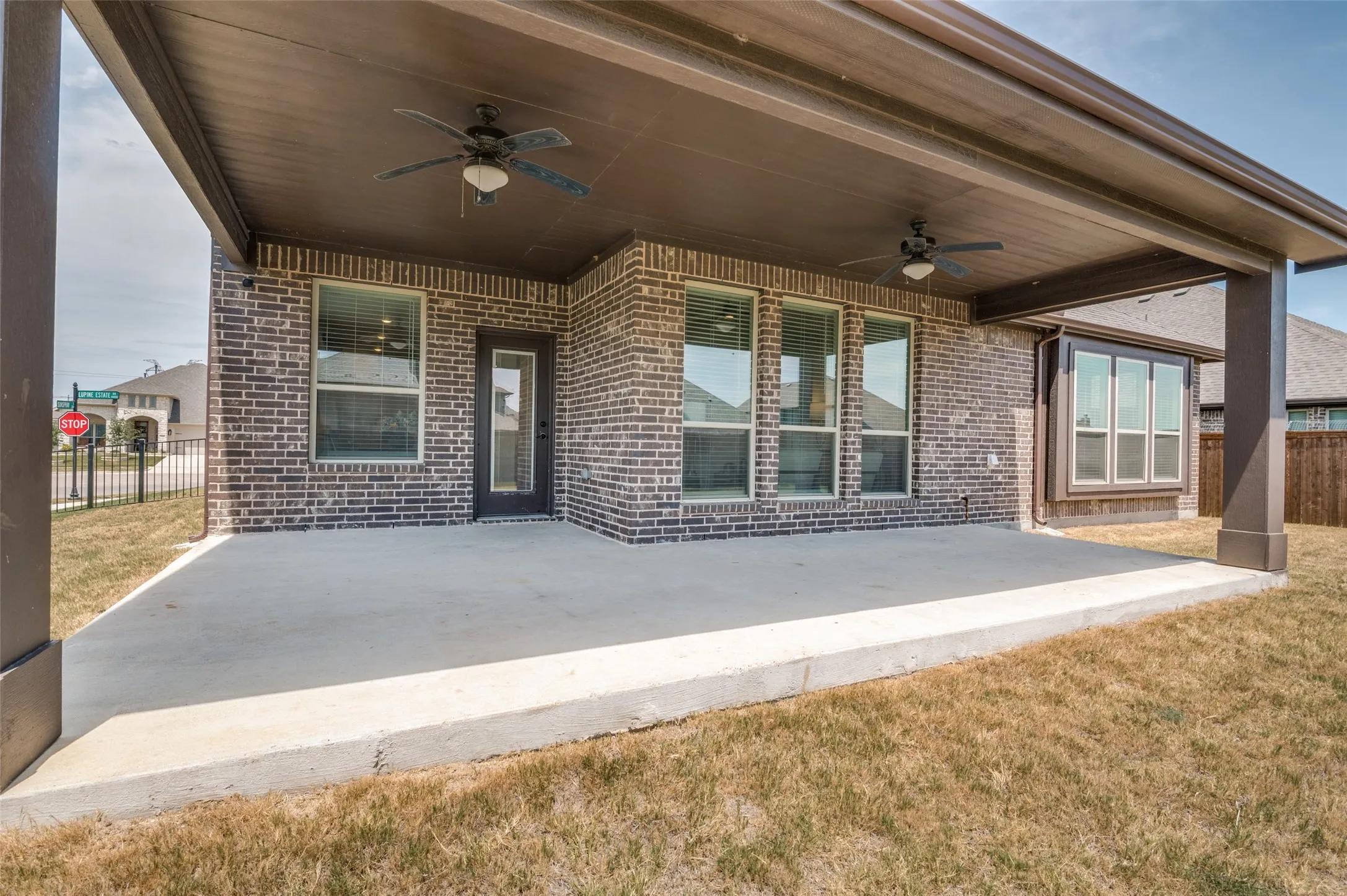 Spacious concrete patio with a dark wood-finish ceiling, two ceiling fans, and brick exterior
