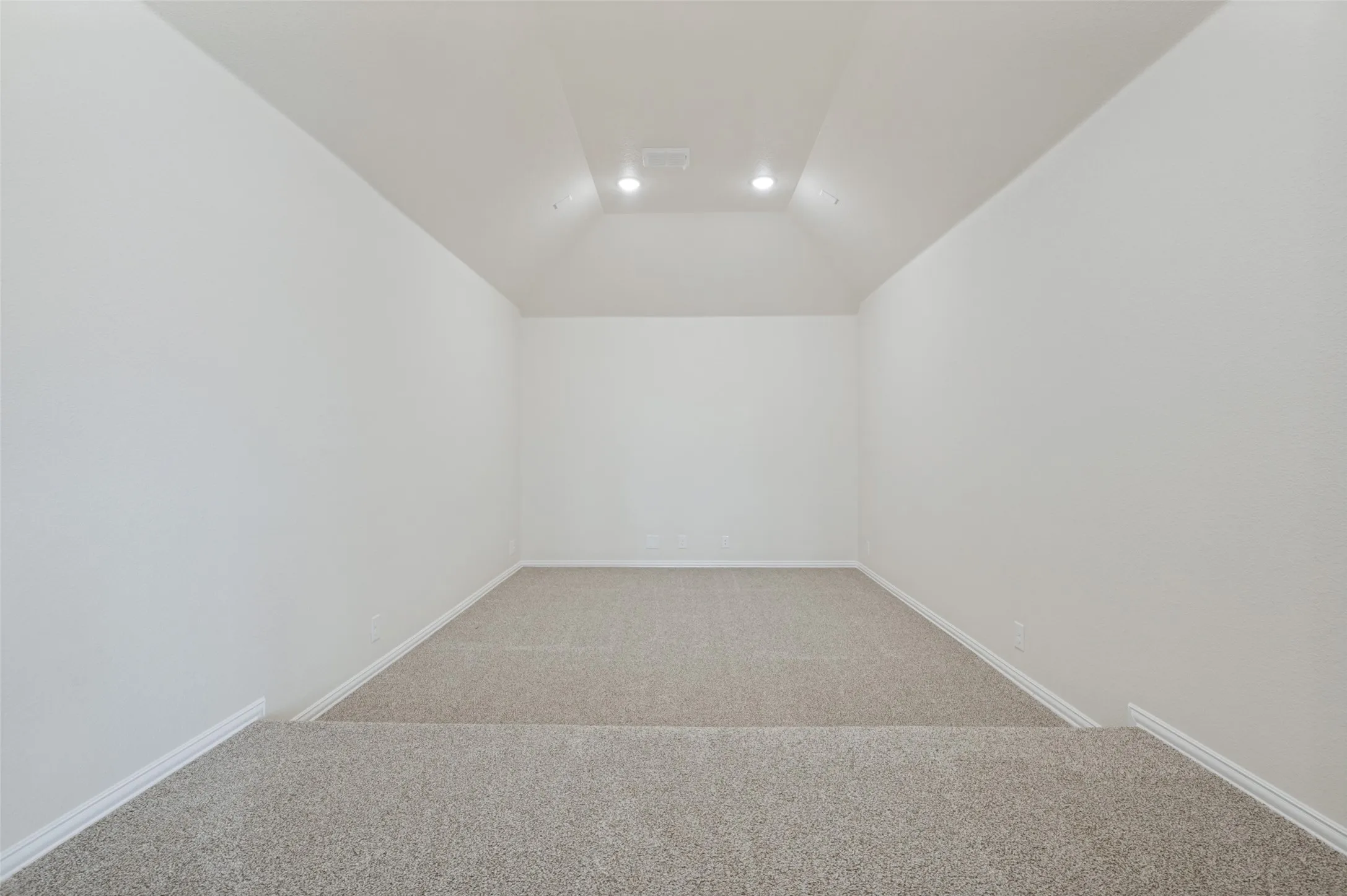 Tiered carpeted flooring with recessed lighting and a vaulted ceiling