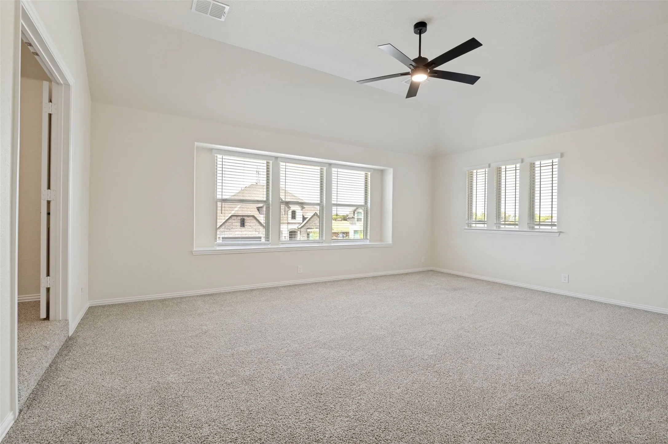 Vaulted ceiling with a ceiling fan, carpeted flooring, and multiple windows with blinds