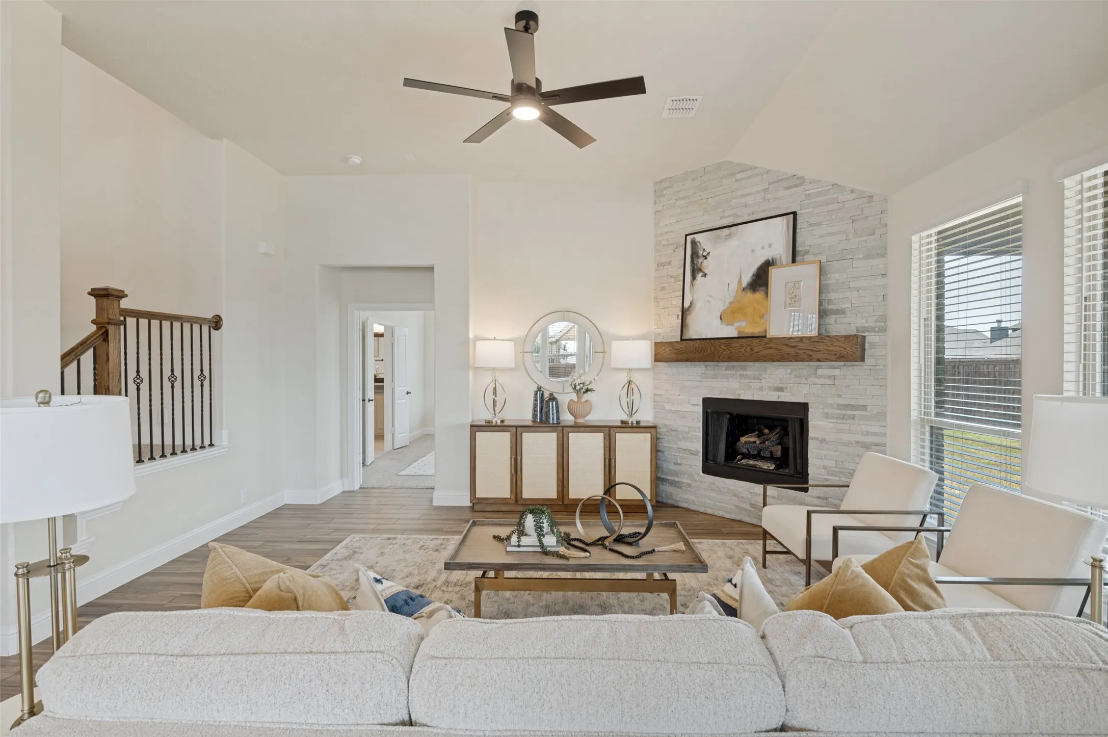 Living area with wood-finish flooring, a contemporary ceiling fan, and a corner fireplace with a stacked stone surround and a wood mantel