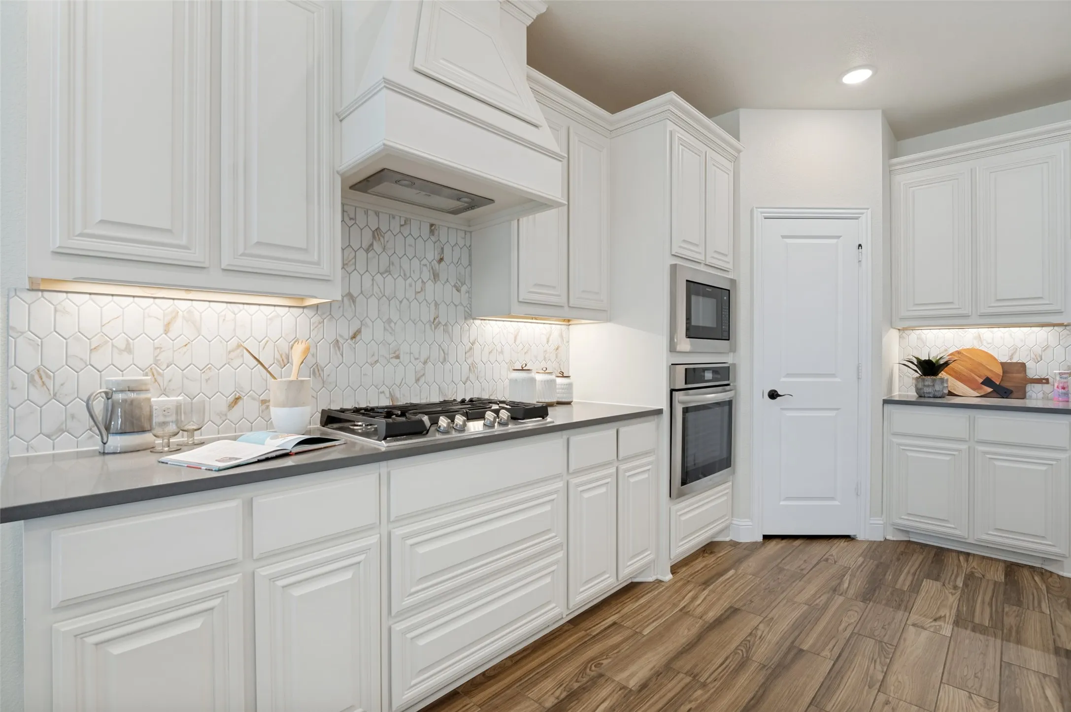 White cabinetry with crown molding, stainless steel built-in appliances, a gas range, a decorative tile backsplash, and wood-finish flooring