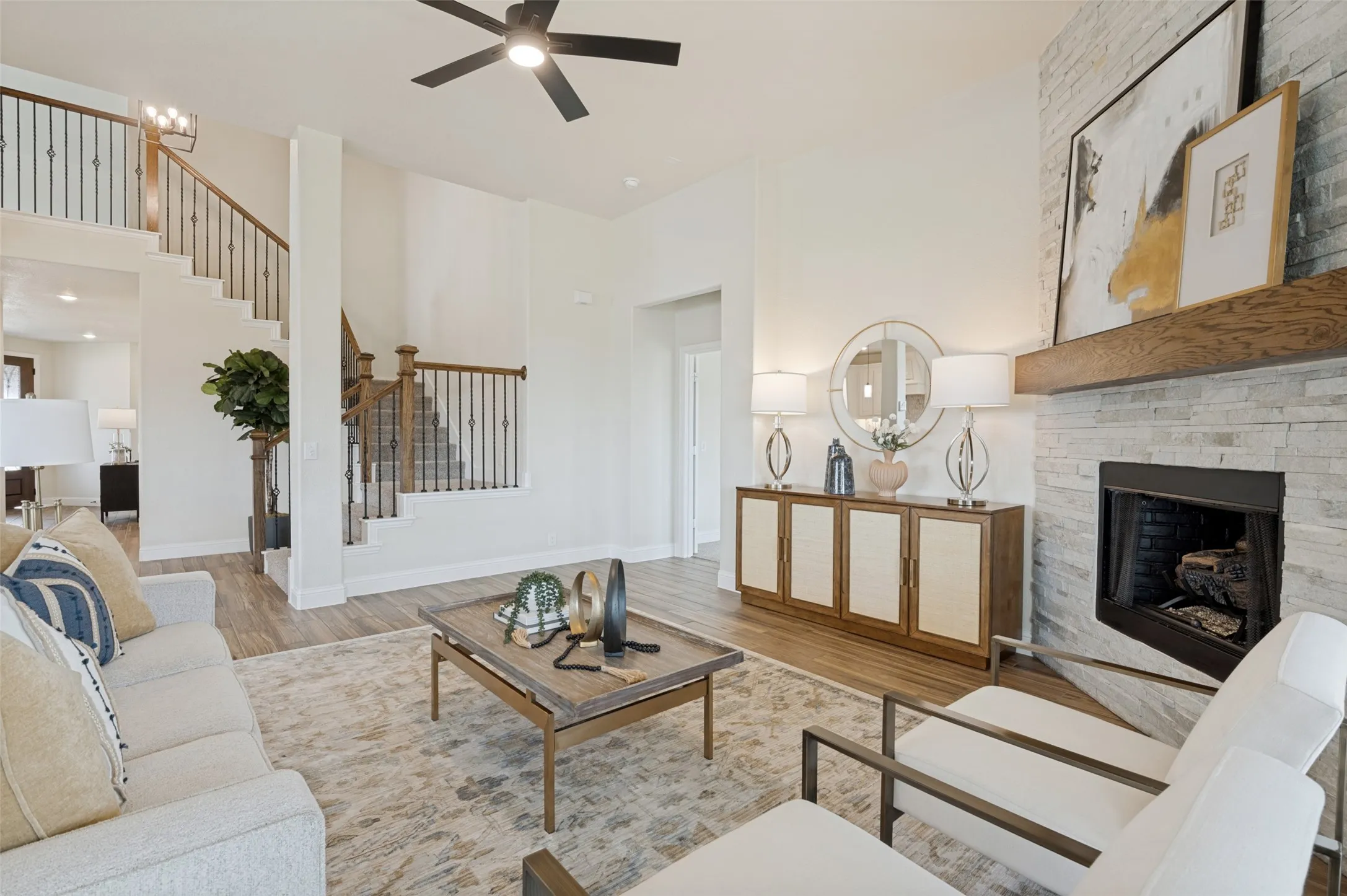 Two-story living area featuring a stone-clad fireplace with a wood mantel, wood-finish flooring, and an open staircase with wrought iron balusters