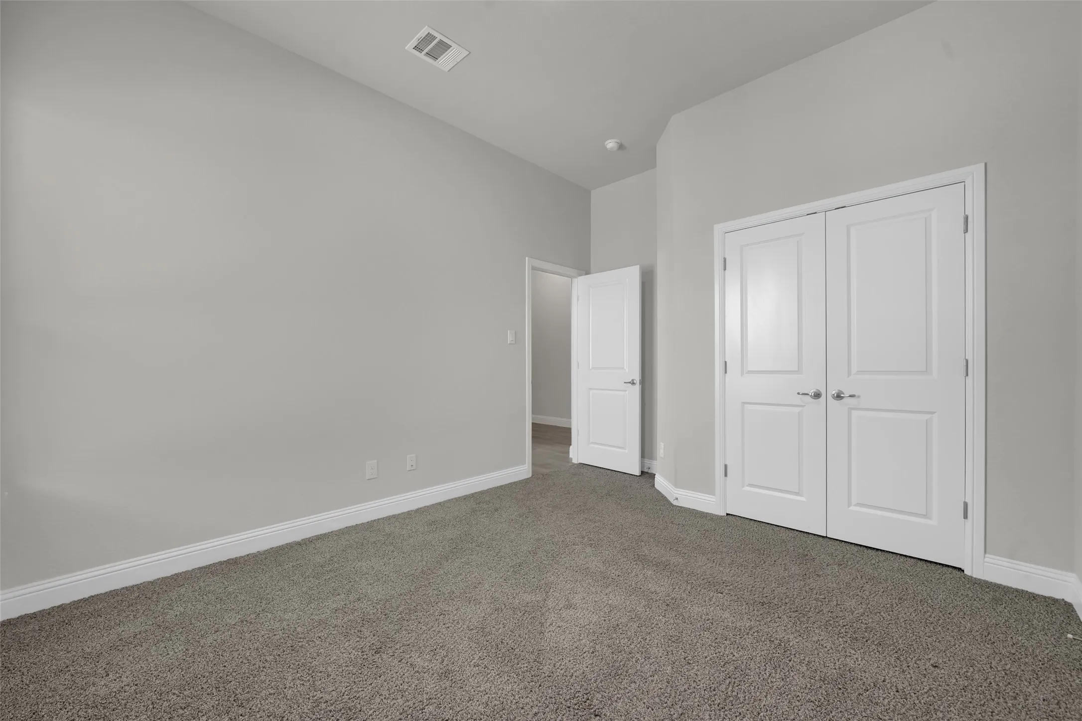 Neutral tone wall paint, grey carpet flooring, white trim, and white paneled doors