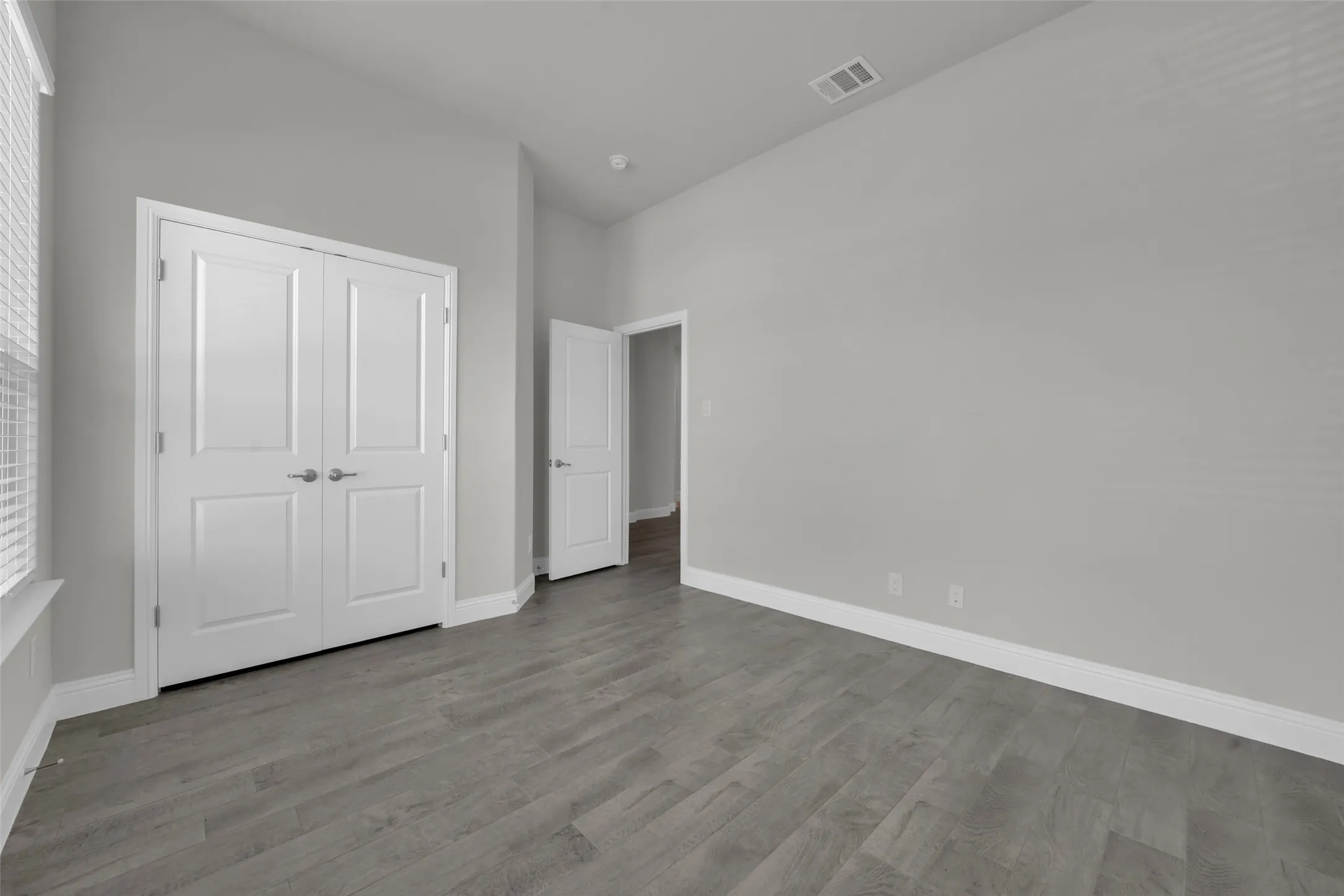 Neutral tone wall paint, wood-finish flooring, white double doors, and white trim