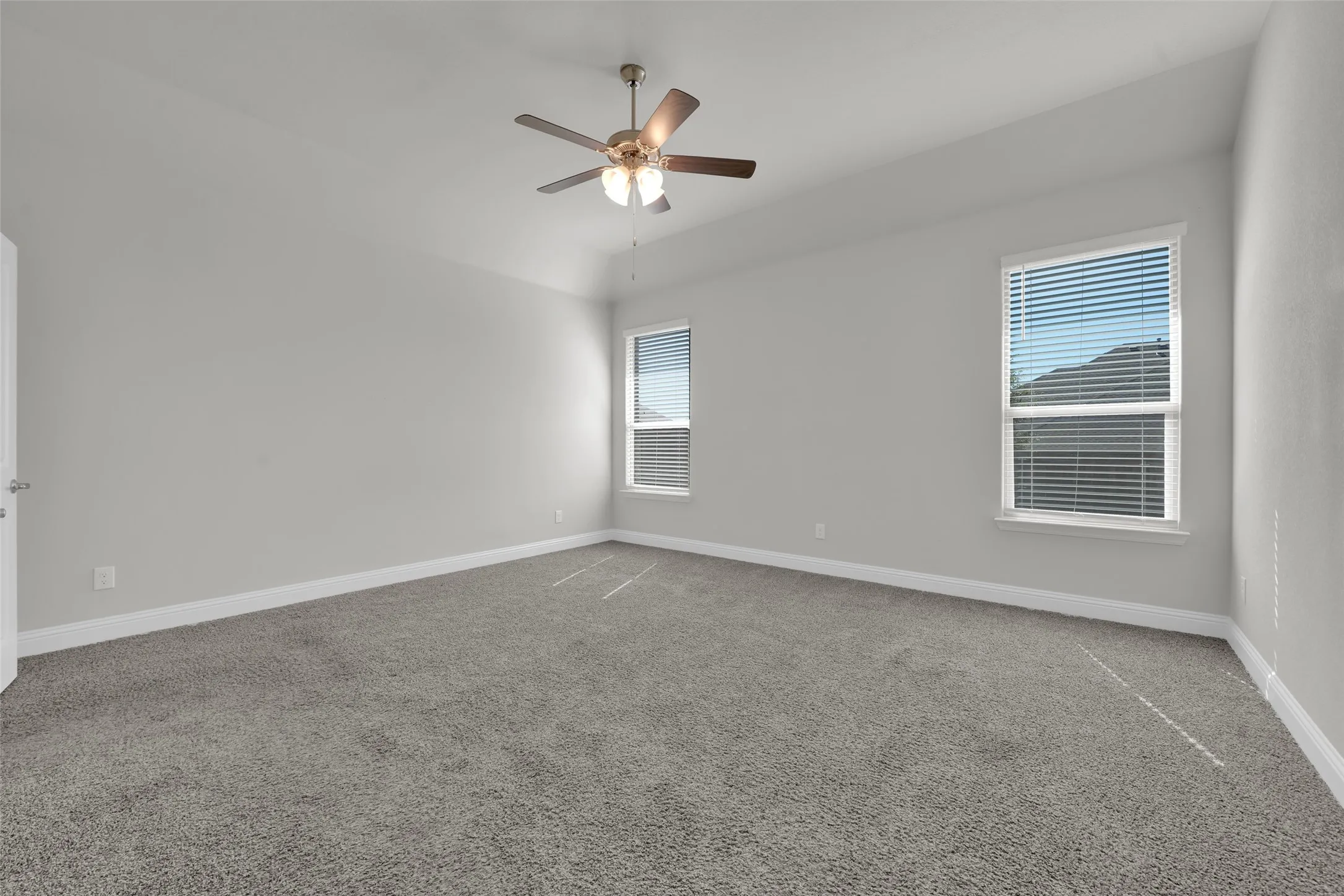 High ceilings, two windows with blinds, gray carpeting, neutral wall color, and a ceiling fan