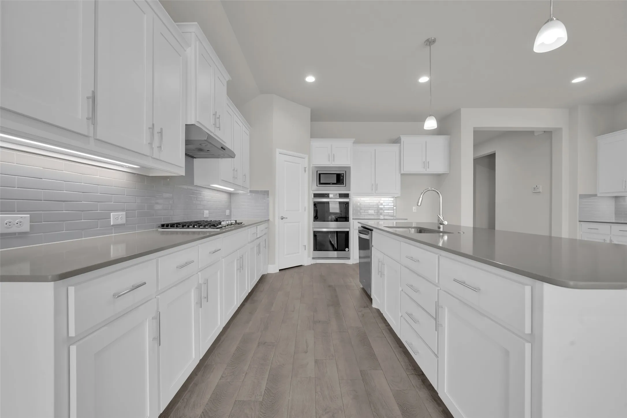 Kitchen featuring white cabinetry, grey subway tile backsplash, stainless steel appliances, and wood-finish flooring