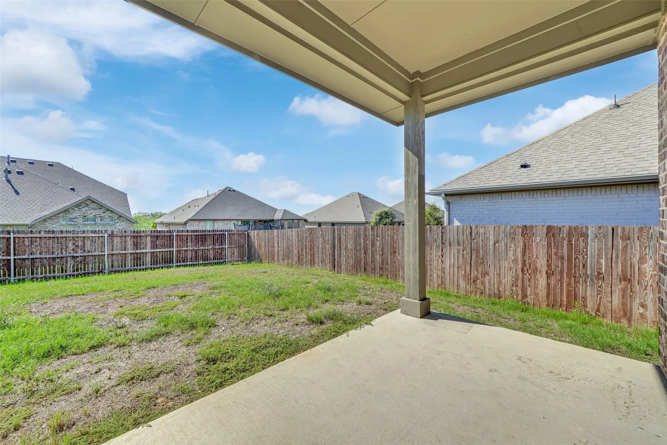 Covered patio with a concrete surface, wooden privacy fence, and expansive grassy yard