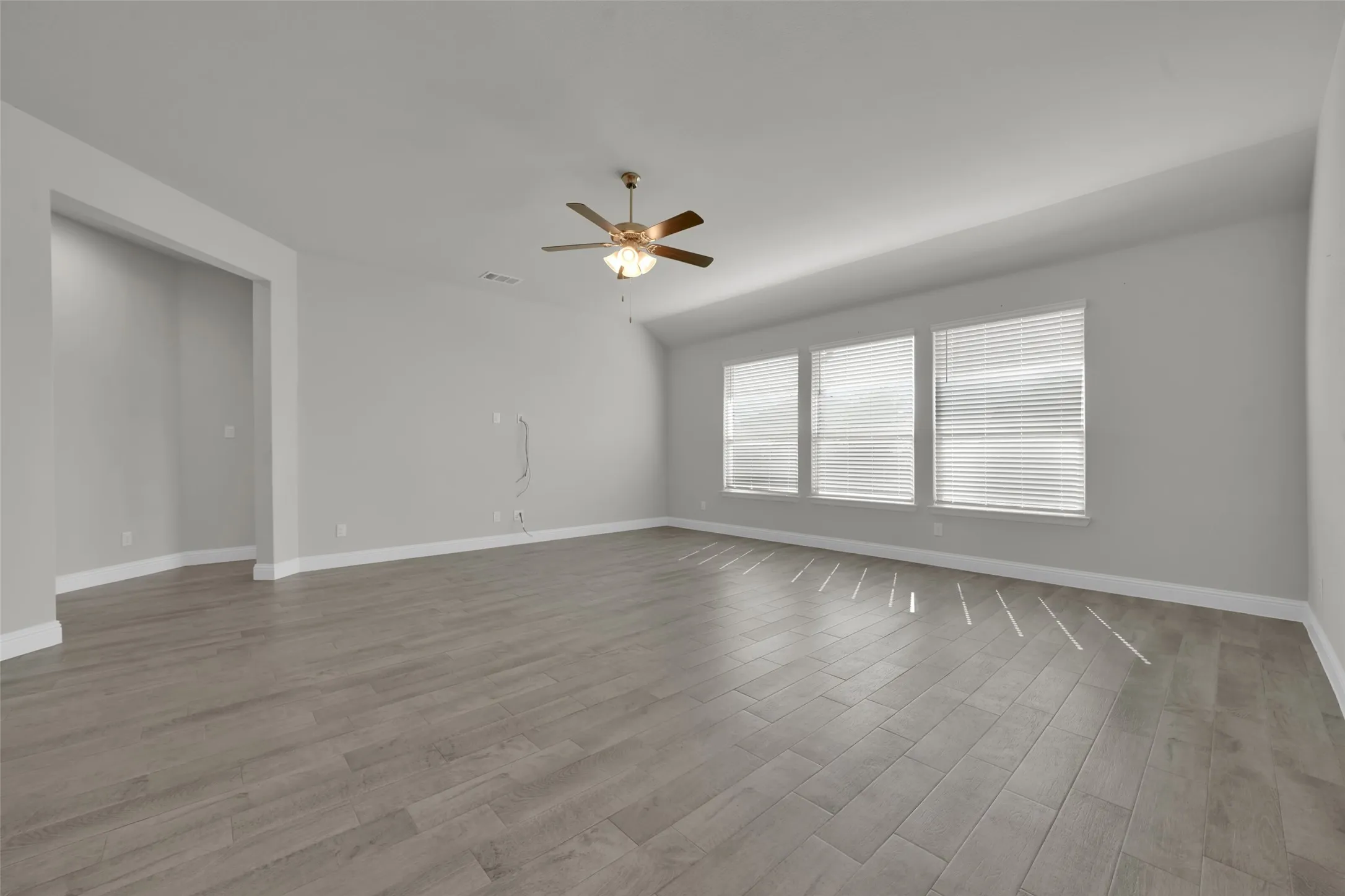 Expansive room featuring wood-look tile flooring, three large windows with blinds, and a ceiling fan with integrated lighting