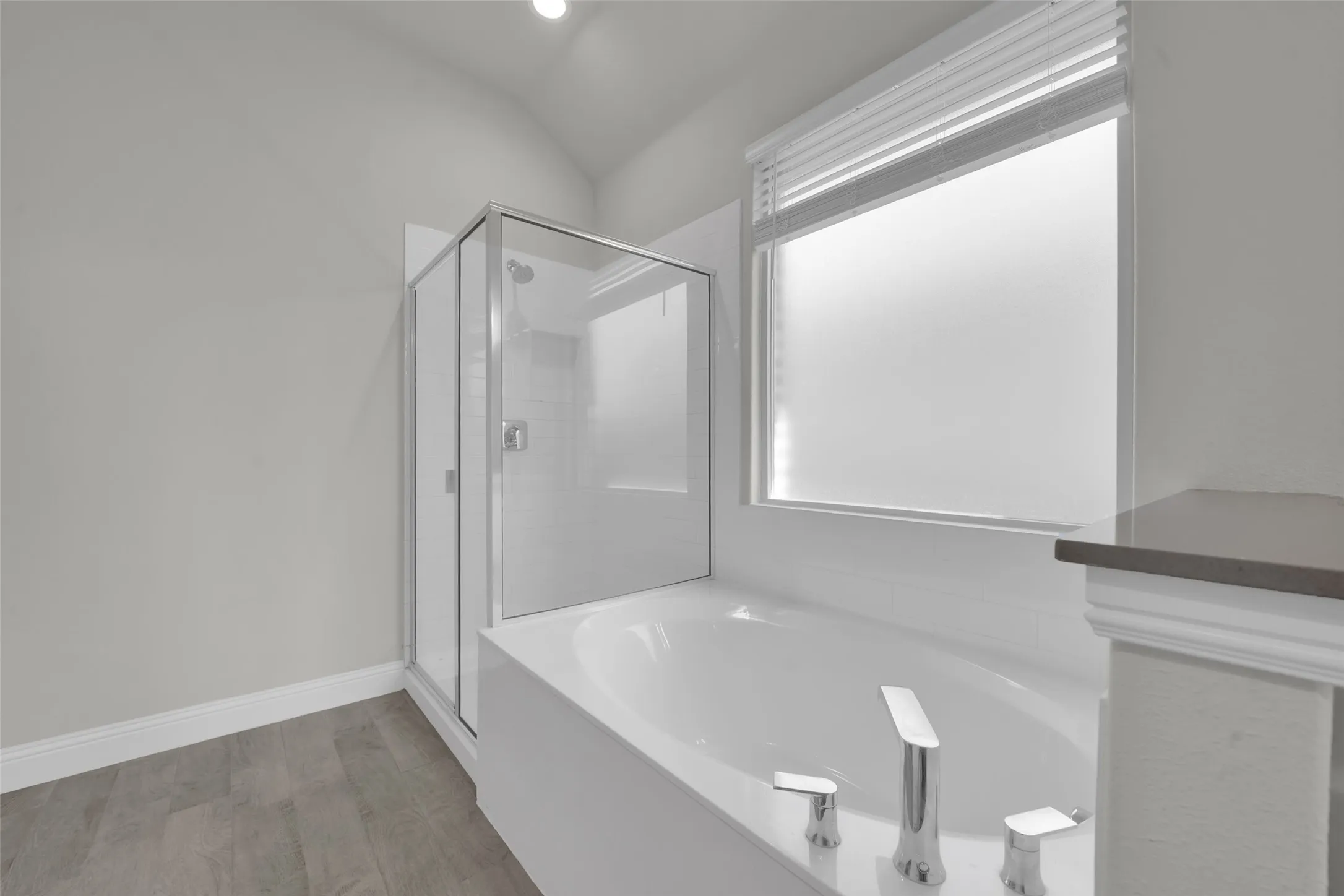 Enclosed shower with clear glass, a built-in tub with deck-mounted fixtures, a privacy window, and wood-finish flooring