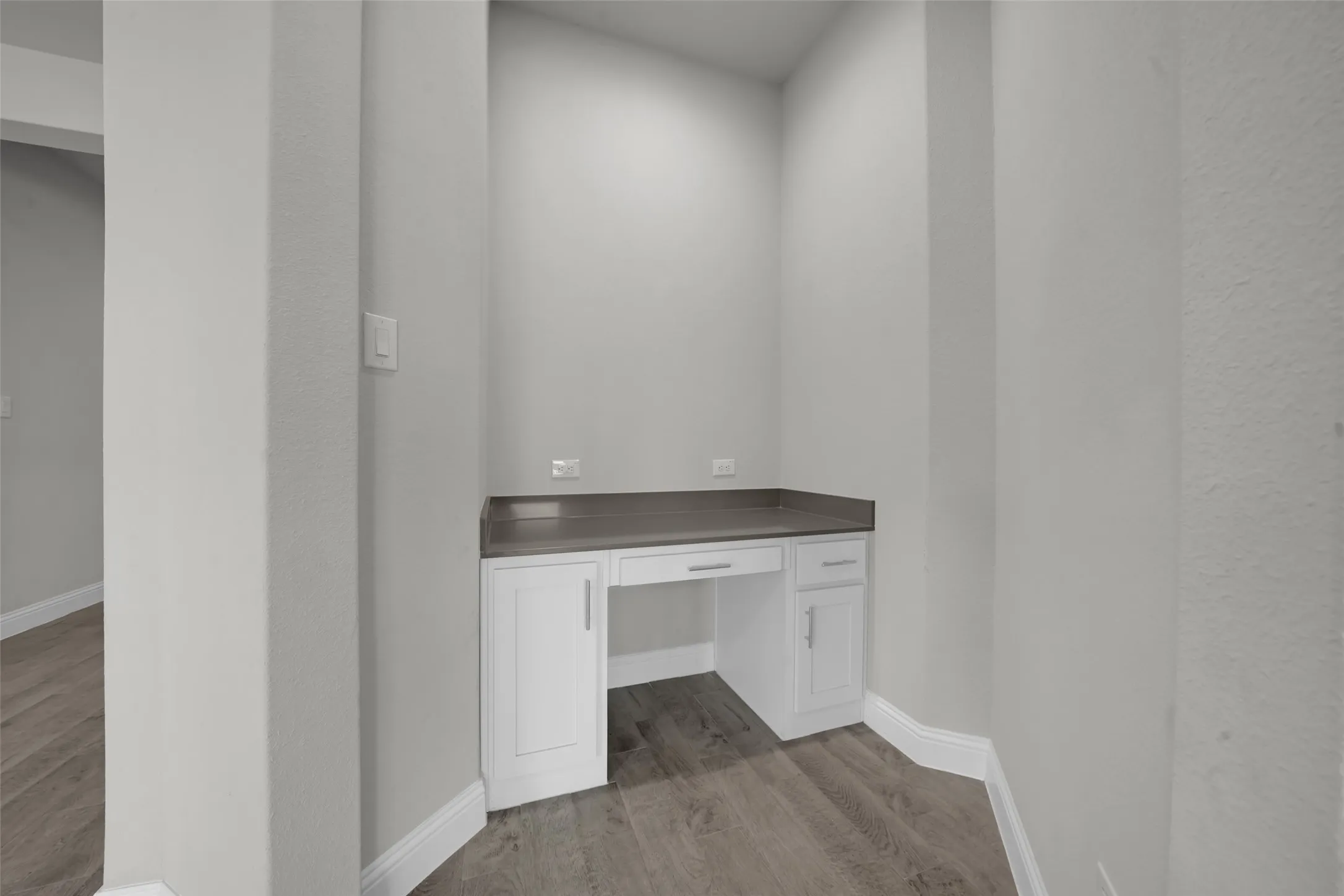 Built-in desk area featuring white cabinetry, a dark countertop, and wood-finish flooring