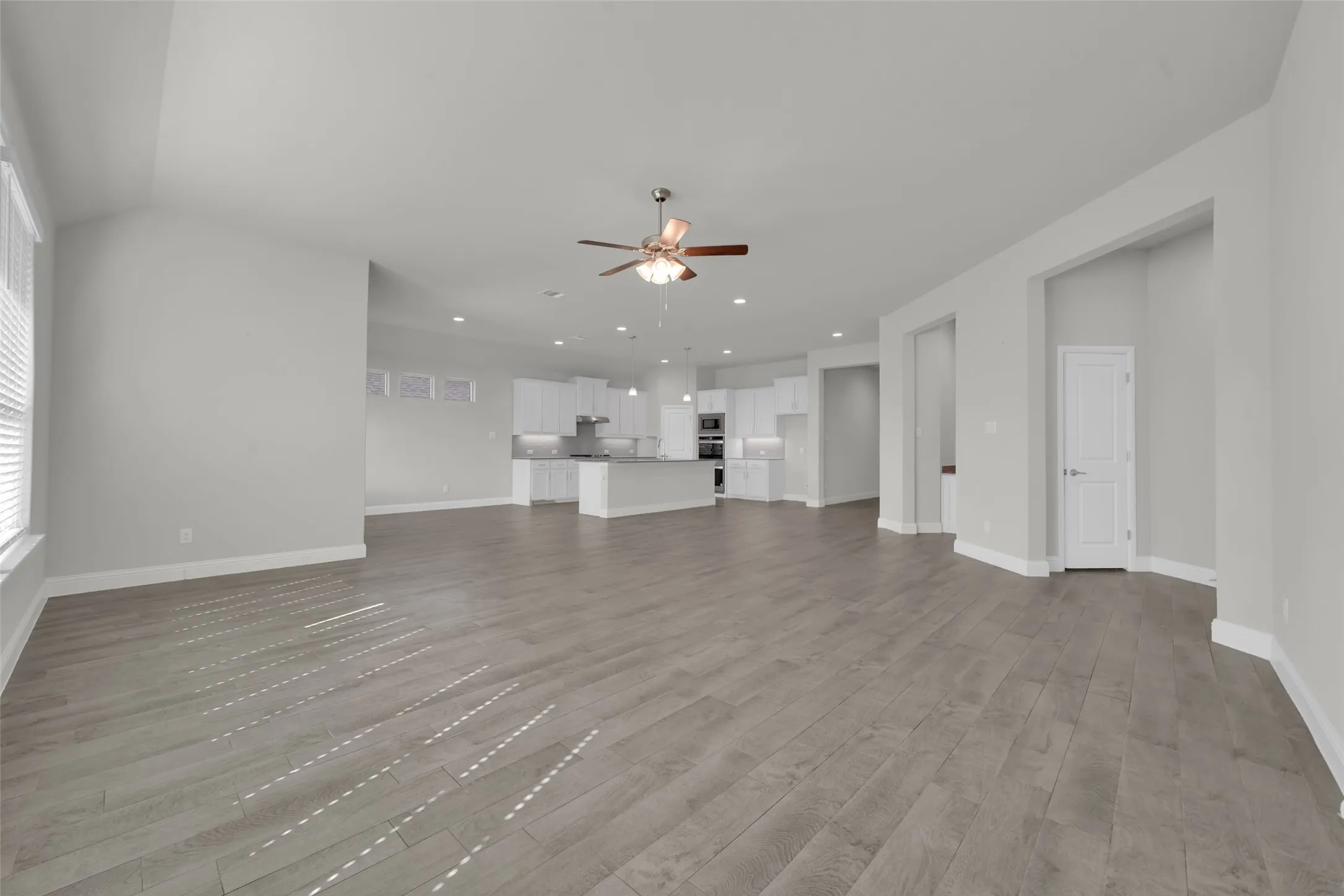 Expansive open-concept living area featuring wood-finish flooring, vaulted ceilings, and a ceiling fan