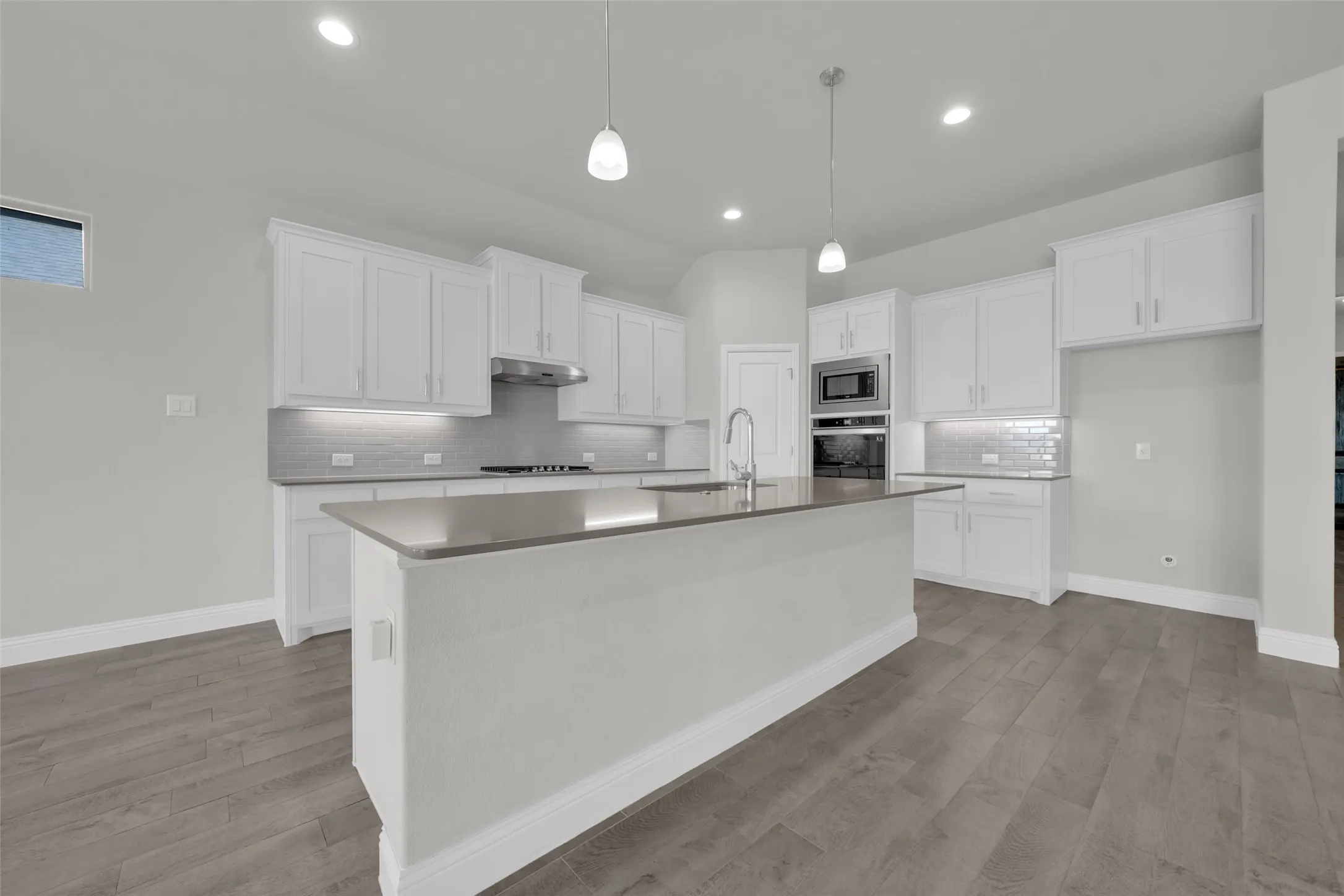 Kitchen featuring a central island, white cabinetry, integrated stainless steel appliances, pendant lighting, and wood-finish flooring