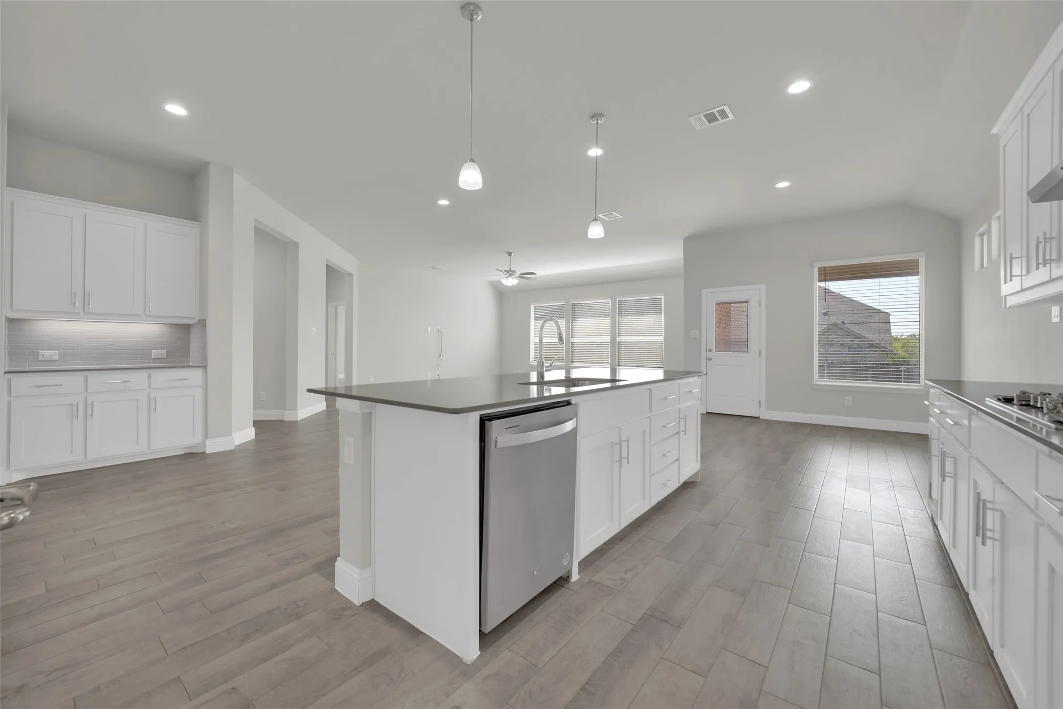 Open concept kitchen featuring an expansive center island, white cabinetry, integrated stainless steel dishwasher, and wood-finish flooring