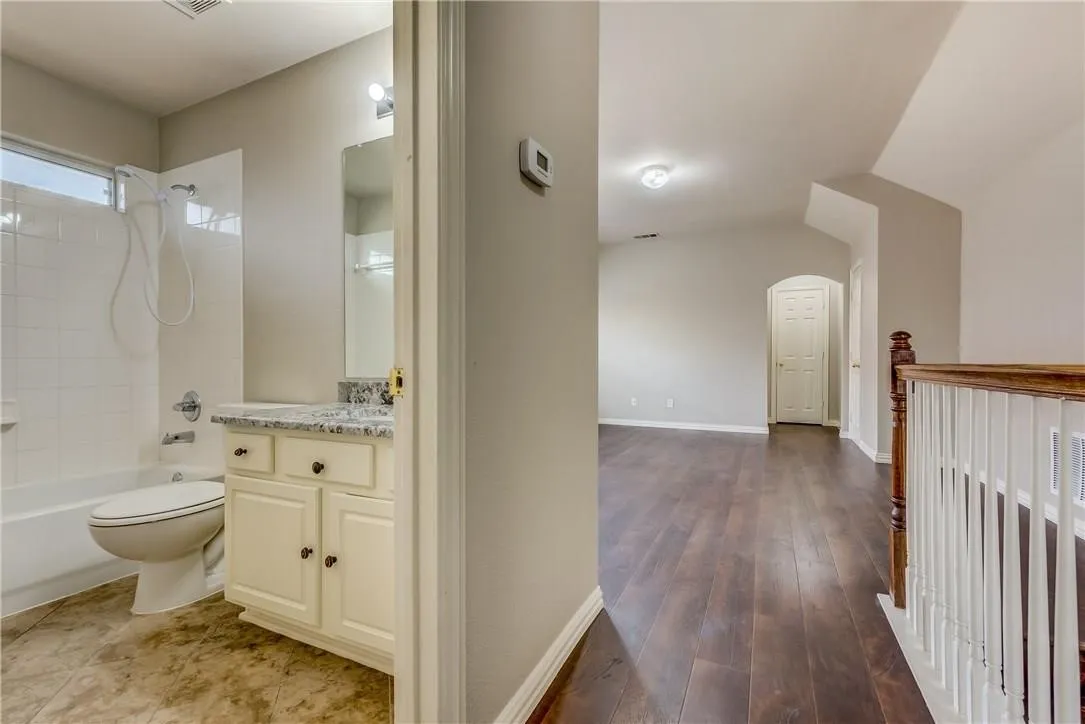 Full bathroom with tiled shower / bath, vaulted ceiling, toilet, wood-type flooring, and vanity