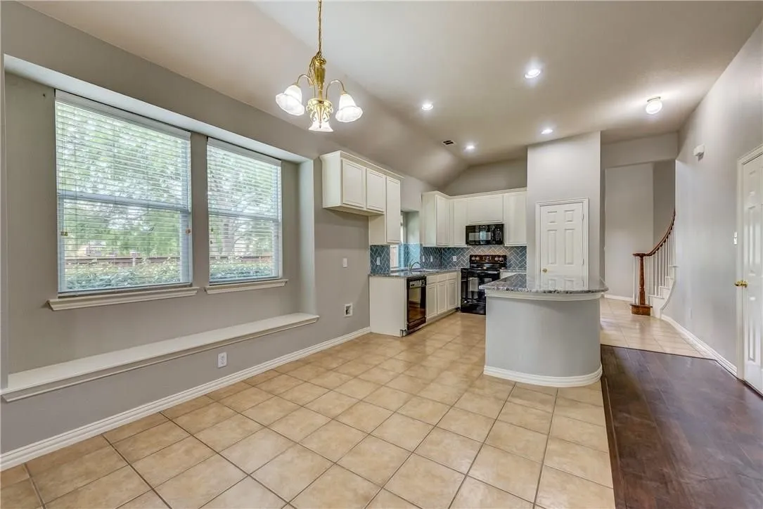 Kitchen featuring light tile floors, backsplash, white cabinetry, black appliances, and vaulted ceiling