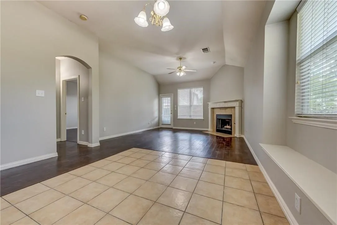 Unfurnished living room featuring vaulted ceiling, ceiling fan with notable chandelier, and light tile floors