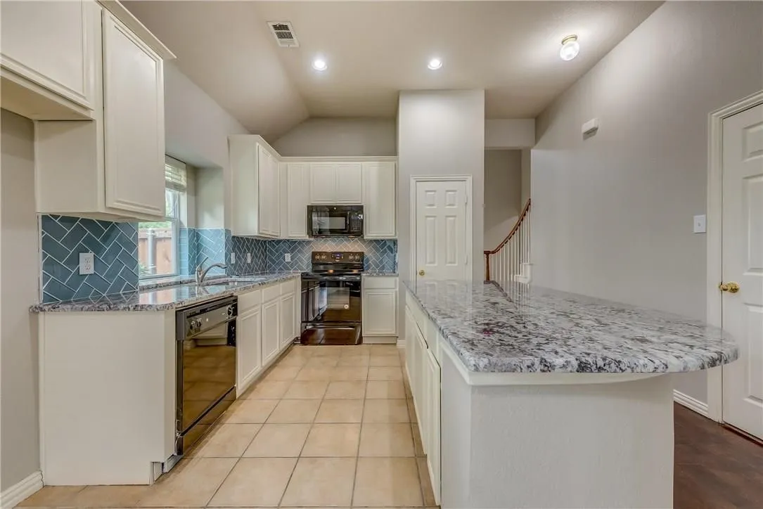 Kitchen with white cabinetry, black appliances, and backsplash
