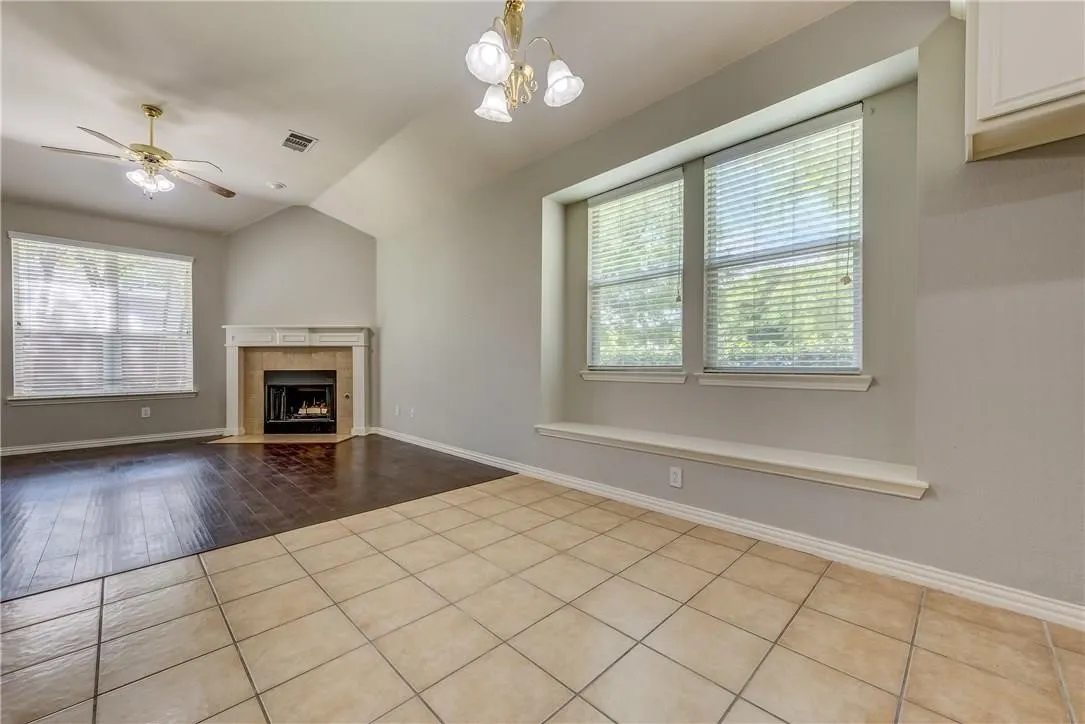 Unfurnished living room with vaulted ceiling, light hardwood / wood-style floors, ceiling fan with notable chandelier, and a tile fireplace
