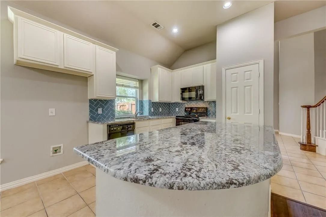 Kitchen with a center island, white cabinetry, black appliances, and tasteful backsplash