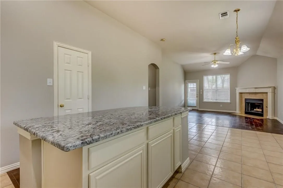 Kitchen with ceiling fan with notable chandelier, a tile fireplace, pendant lighting, a center island, and light tile floors