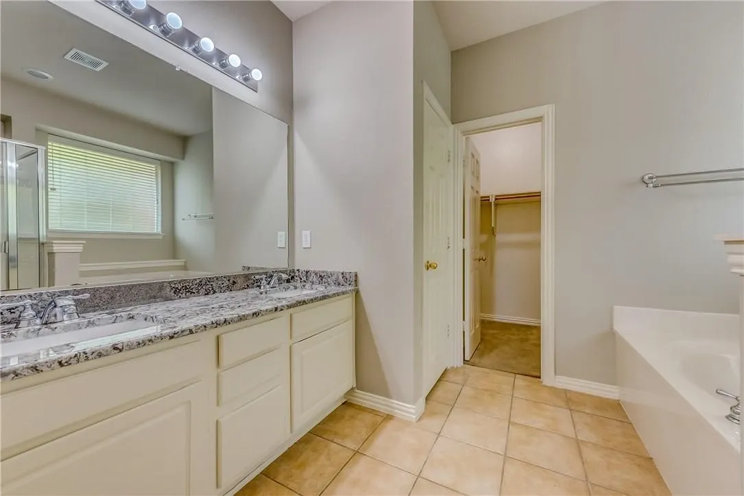 Bathroom with dual sinks, large vanity, tile floors, and plus walk in shower