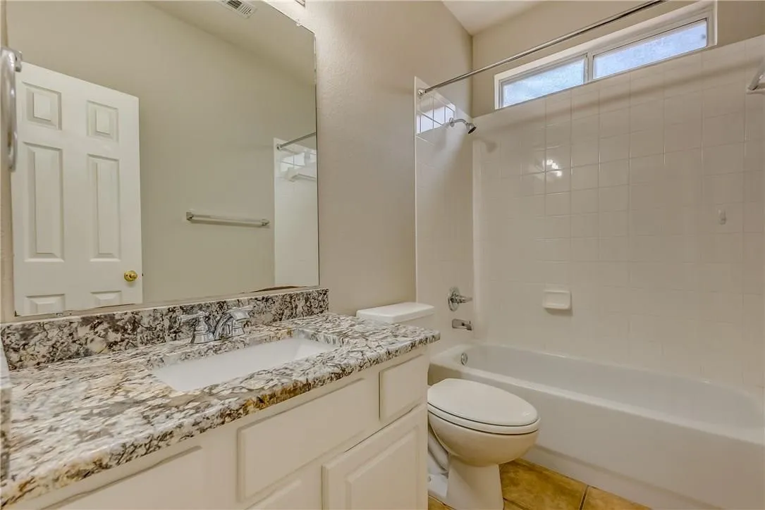 Full bathroom with tiled shower / bath, toilet, tile flooring, and vanity