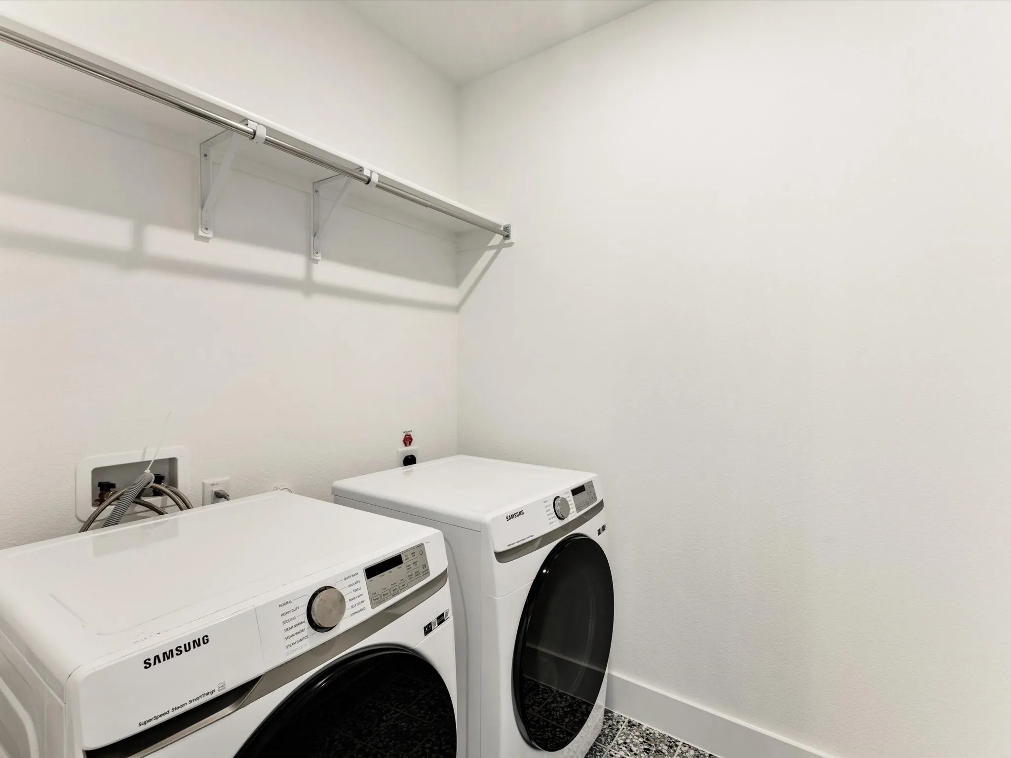 Laundry area with white walls, a storage shelf, and a speckled floor