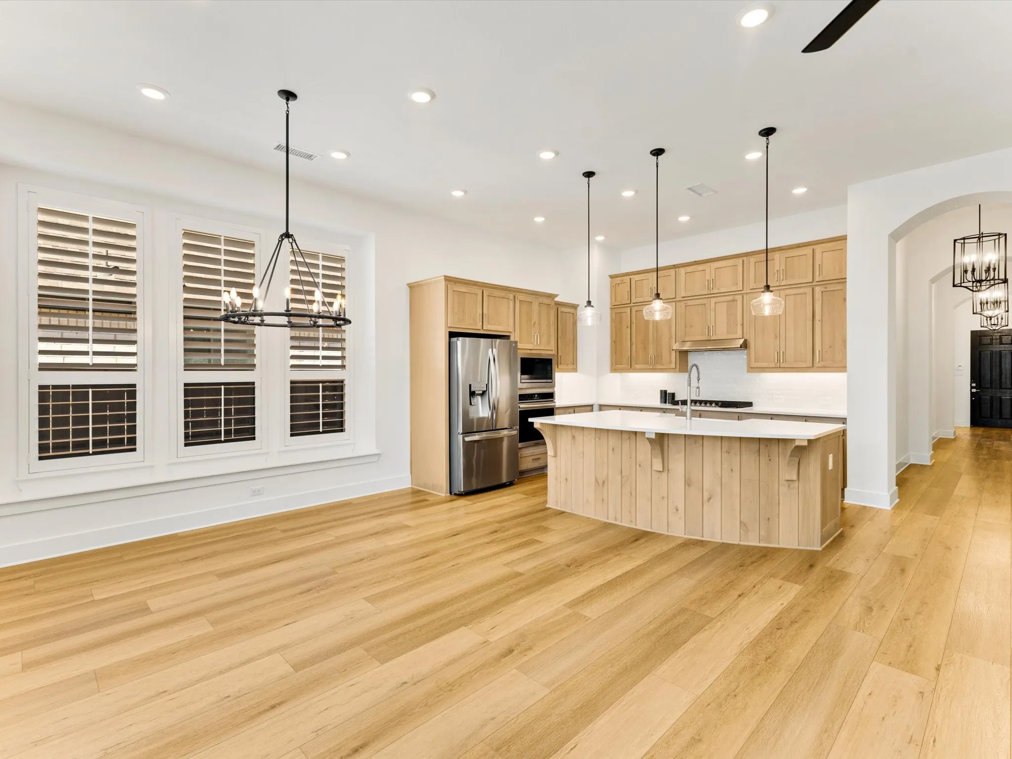 Expansive wood-finish flooring throughout, kitchen featuring light wood cabinetry, a central island with a solid surface countertop, stainless steel appliances, and recessed lighting