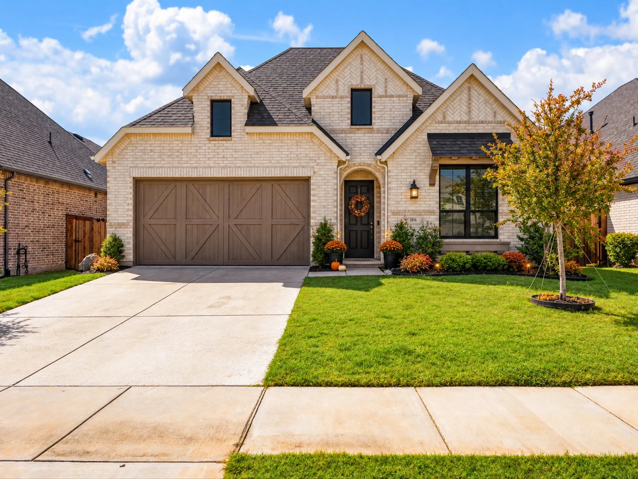 Light-toned brick exterior with stone accents, dark frame windows, an attached two-car garage with a wood-finish door, and a concrete driveway