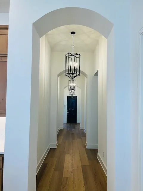 Hallway featuring arched doorways, wood-finish flooring, and suspended pendant lighting