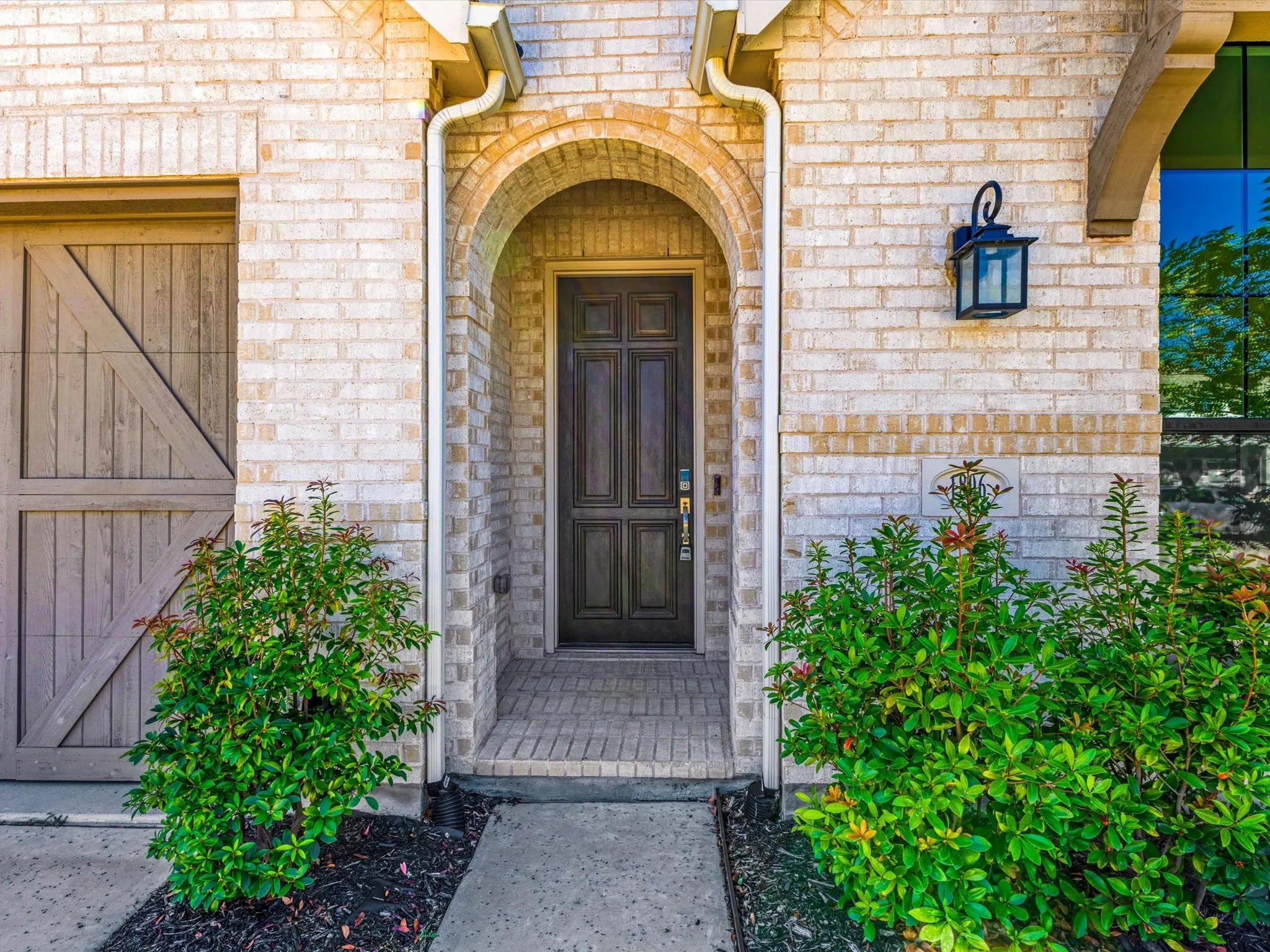 Brick exterior with an arched entryway, dark wood-paneled door, and a decorative wall-mounted lantern