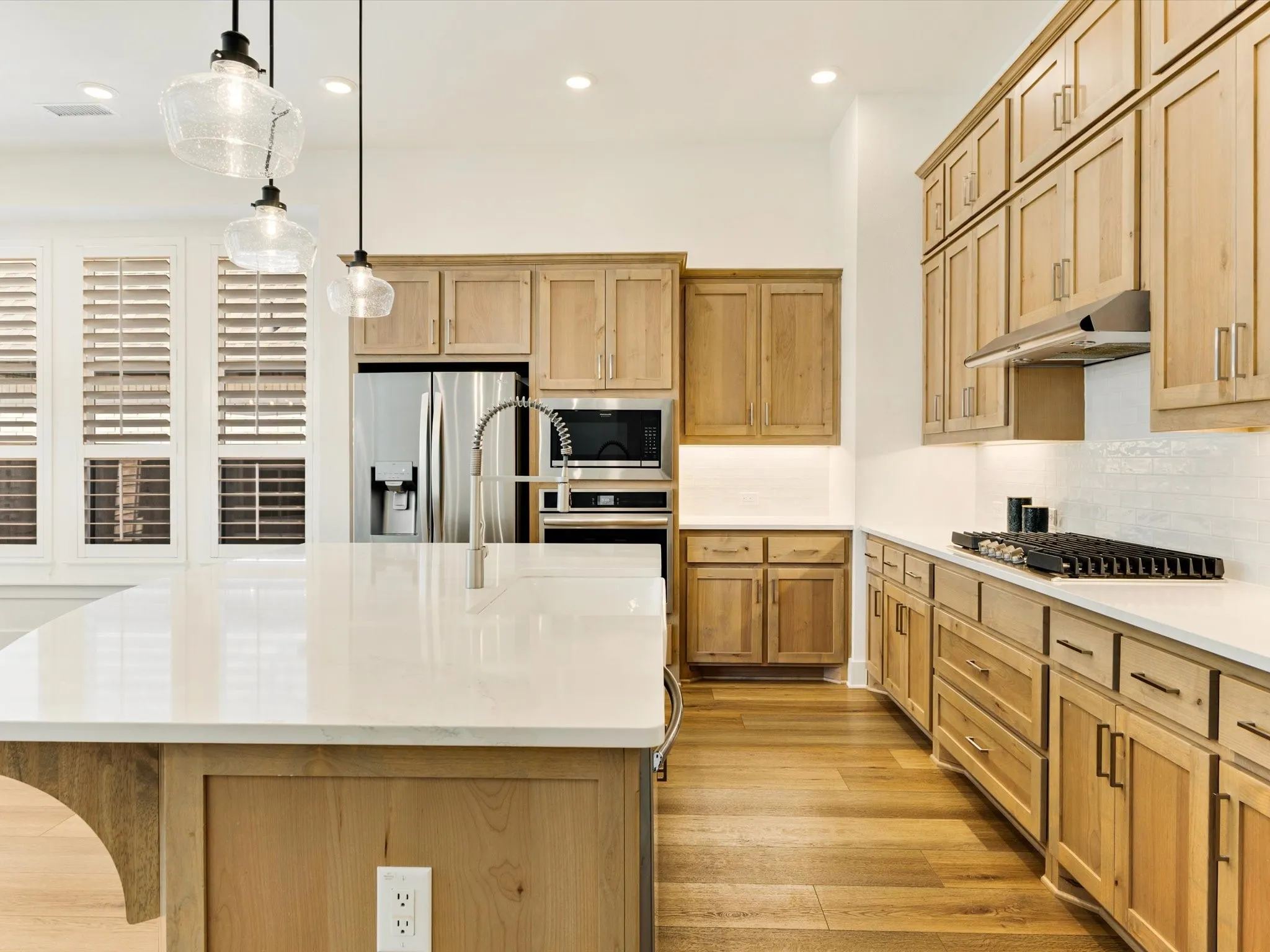 Spacious kitchen featuring light wood-finish cabinetry, stainless steel appliances, a center island with a gooseneck faucet, white countertops, and a white tile backsplash