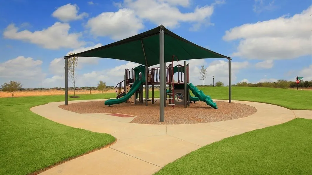 Community playground featuring a multi-level structure with slides, a shade canopy, and surrounded by a concrete pathway