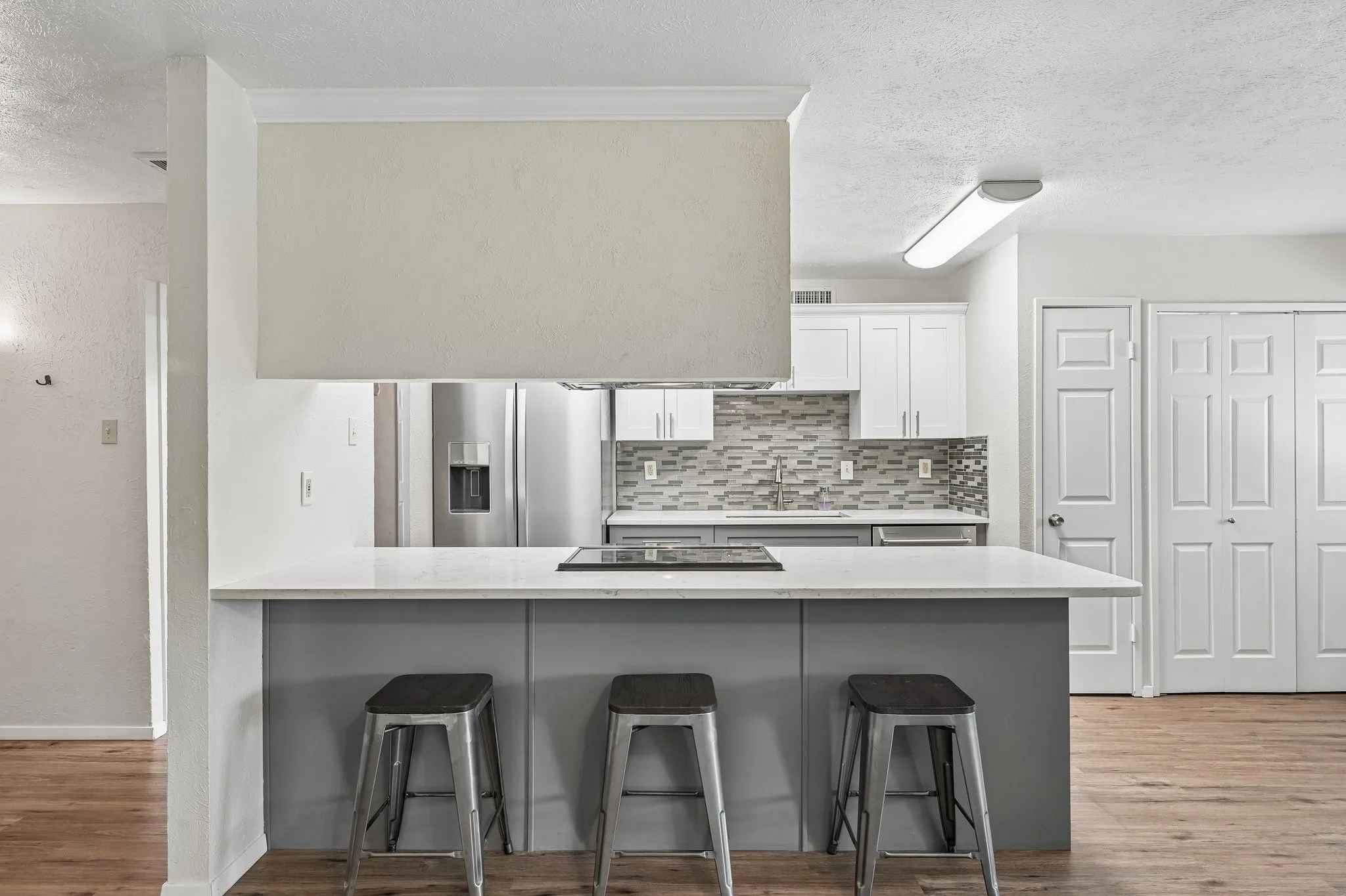 Kitchen with an expansive island and integrated cooktop, stainless steel appliances, mosaic tile backsplash, and two-tone cabinetry