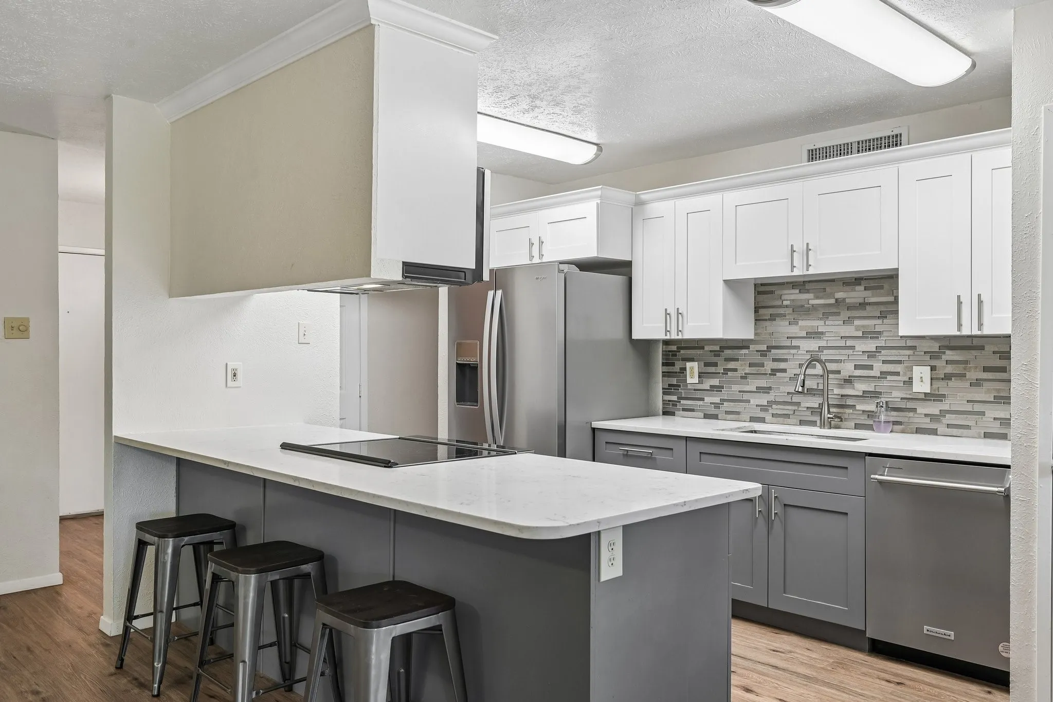 Kitchen featuring a stainless steel refrigerator, stainless steel dishwasher, integrated cooktop, dual-toned cabinetry, and a mosaic tile backsplash