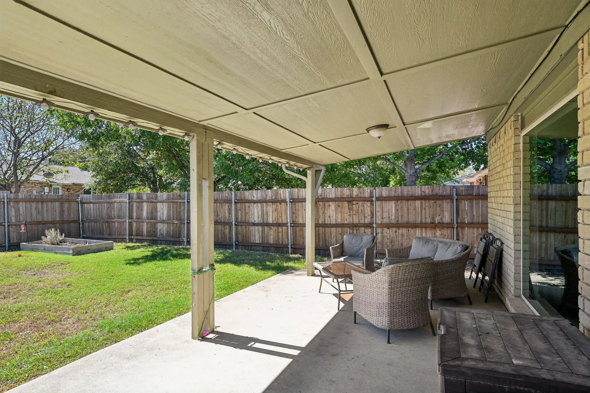 Expansive covered patio with concrete flooring, overlooking a fenced backyard with a raised garden bed