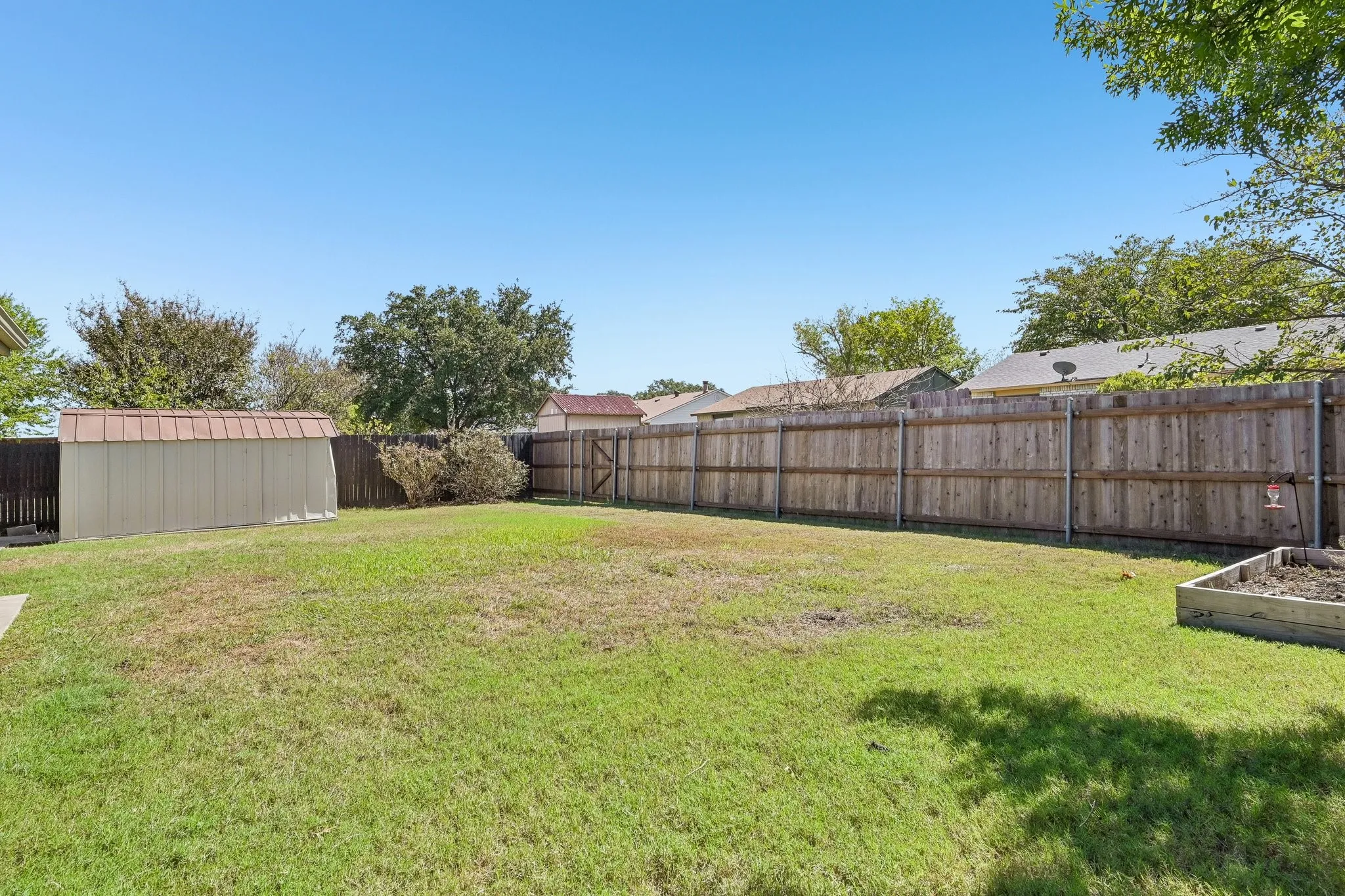 Expansive backyard featuring a wood privacy fence, a storage shed with a metal roof, and a raised garden bed