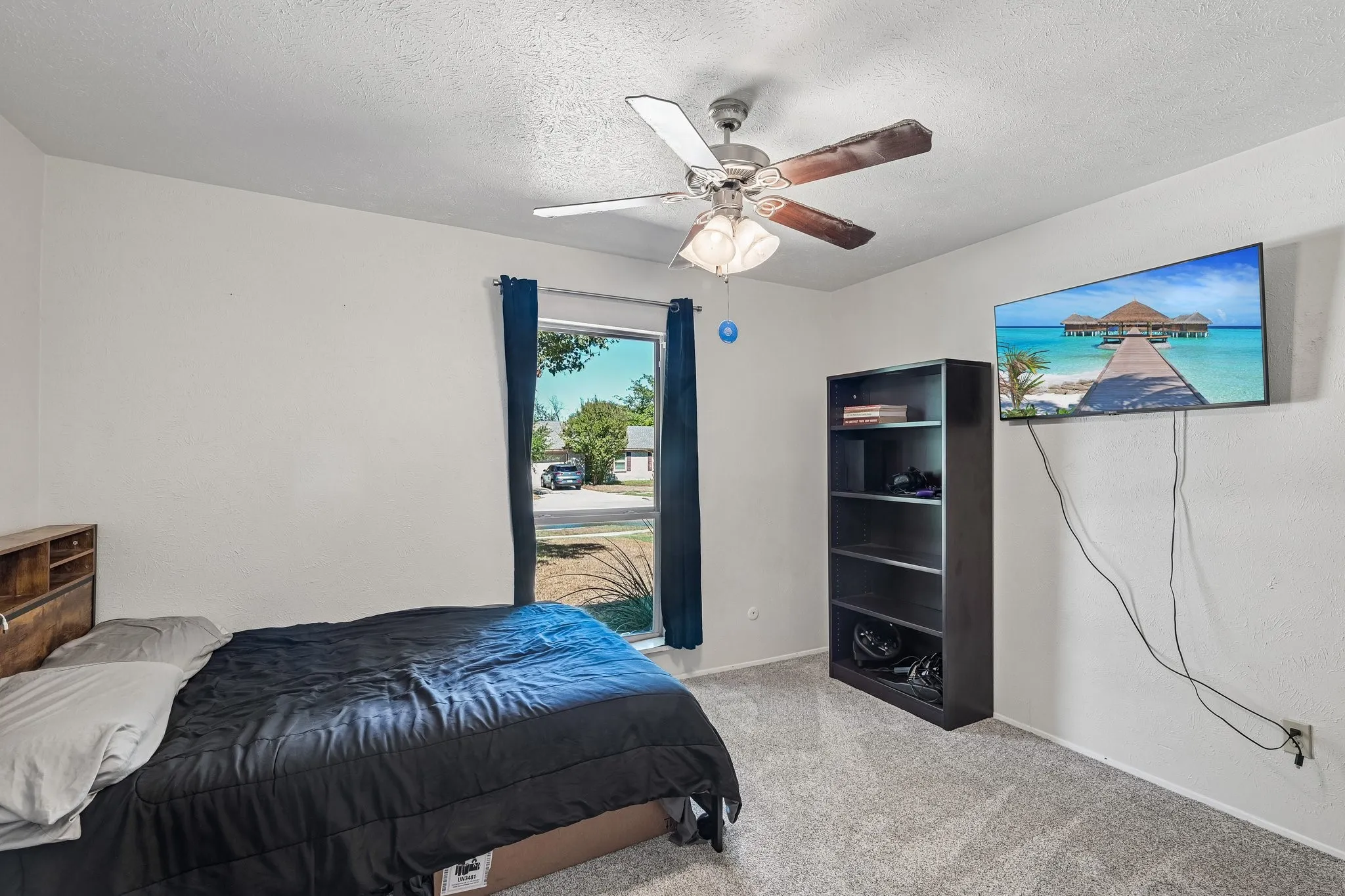 Neutral wall paint, carpet flooring, a ceiling fan with integrated lighting, and a window with curtains