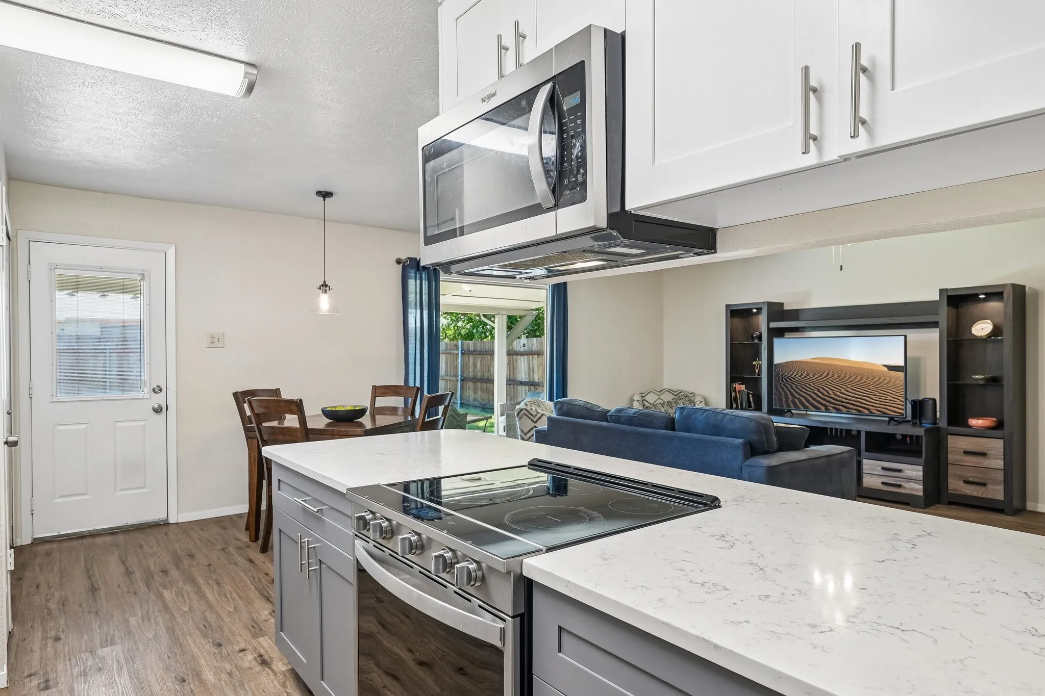 Open-concept kitchen featuring an island with a built-in electric range, white upper cabinetry, and stainless steel appliances