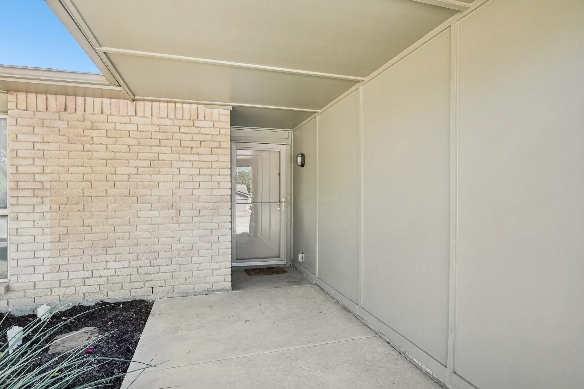 Covered entryway with light brick facade, concrete walkway, and exterior wall sconce